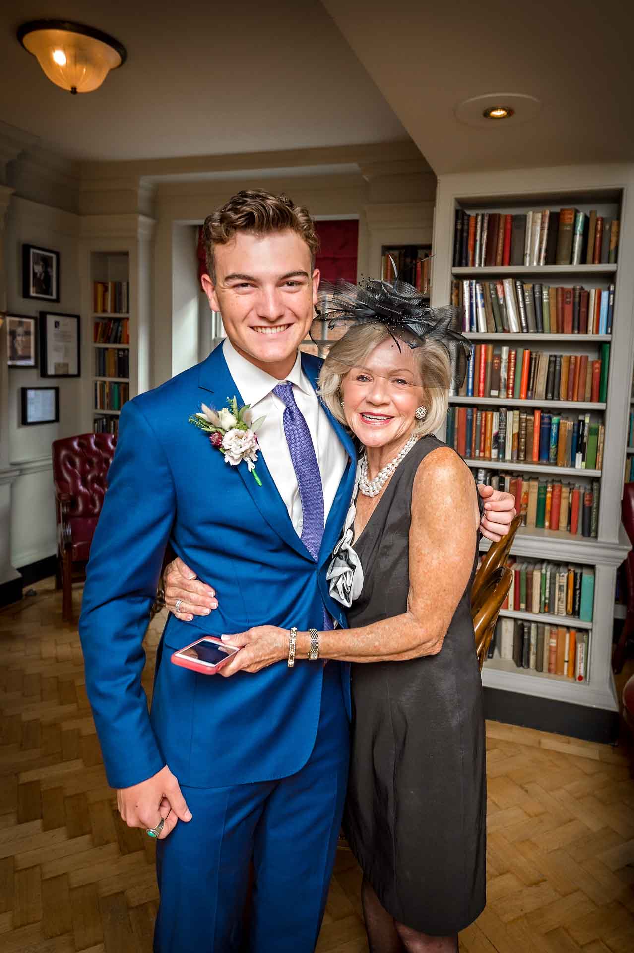 Lady with arms round man in blue suit and holding a phone at wedding