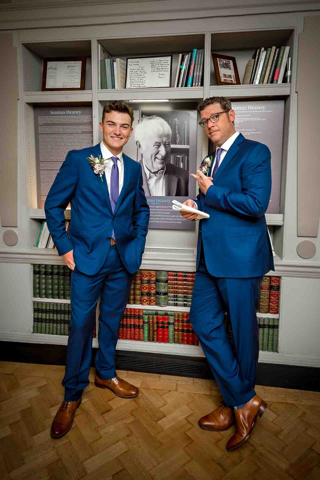 Groom and groomsman standing in front of portrait of Seamus Heaney in the Bloomsbury Hotel