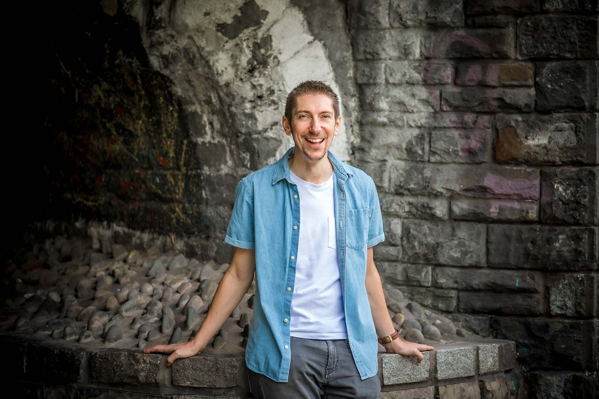 Man with open blue shirt smiling and leaning/sitting on wall in Cardiff
