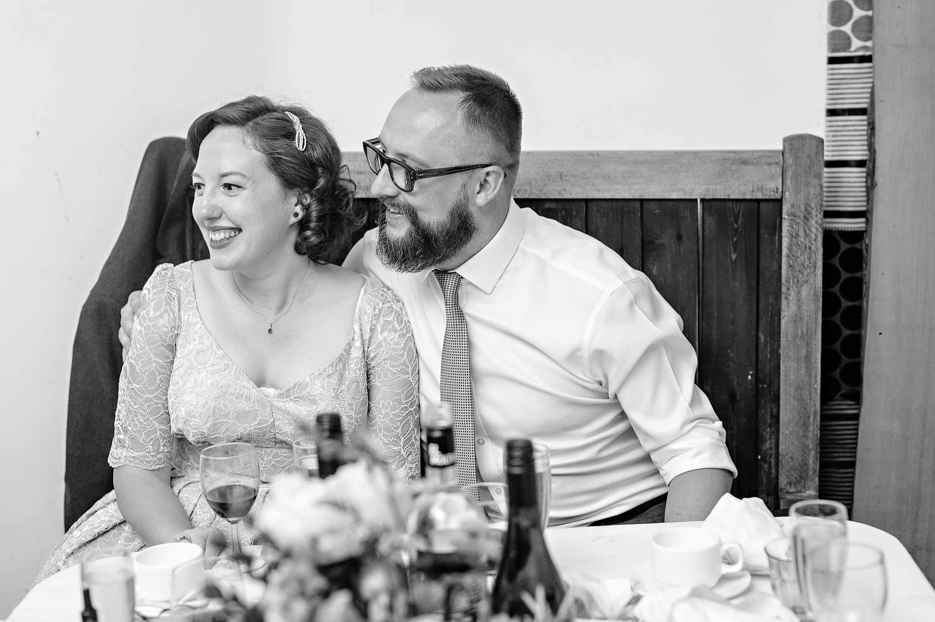 Bride and bearded groom laughing at their wedding breakfast meal
