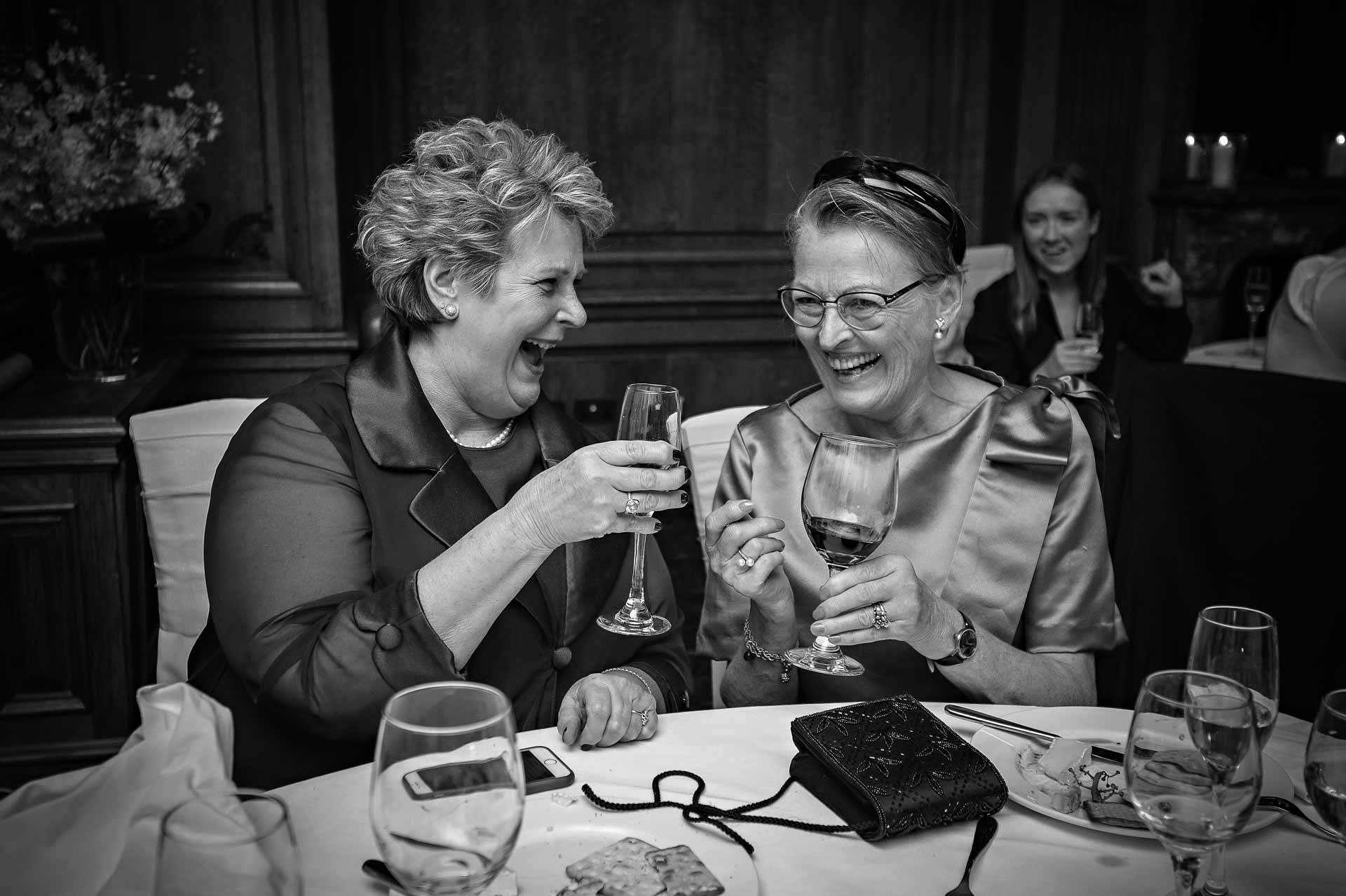 Two ladies laughing at wedding breakfast meal holding wine glasses
