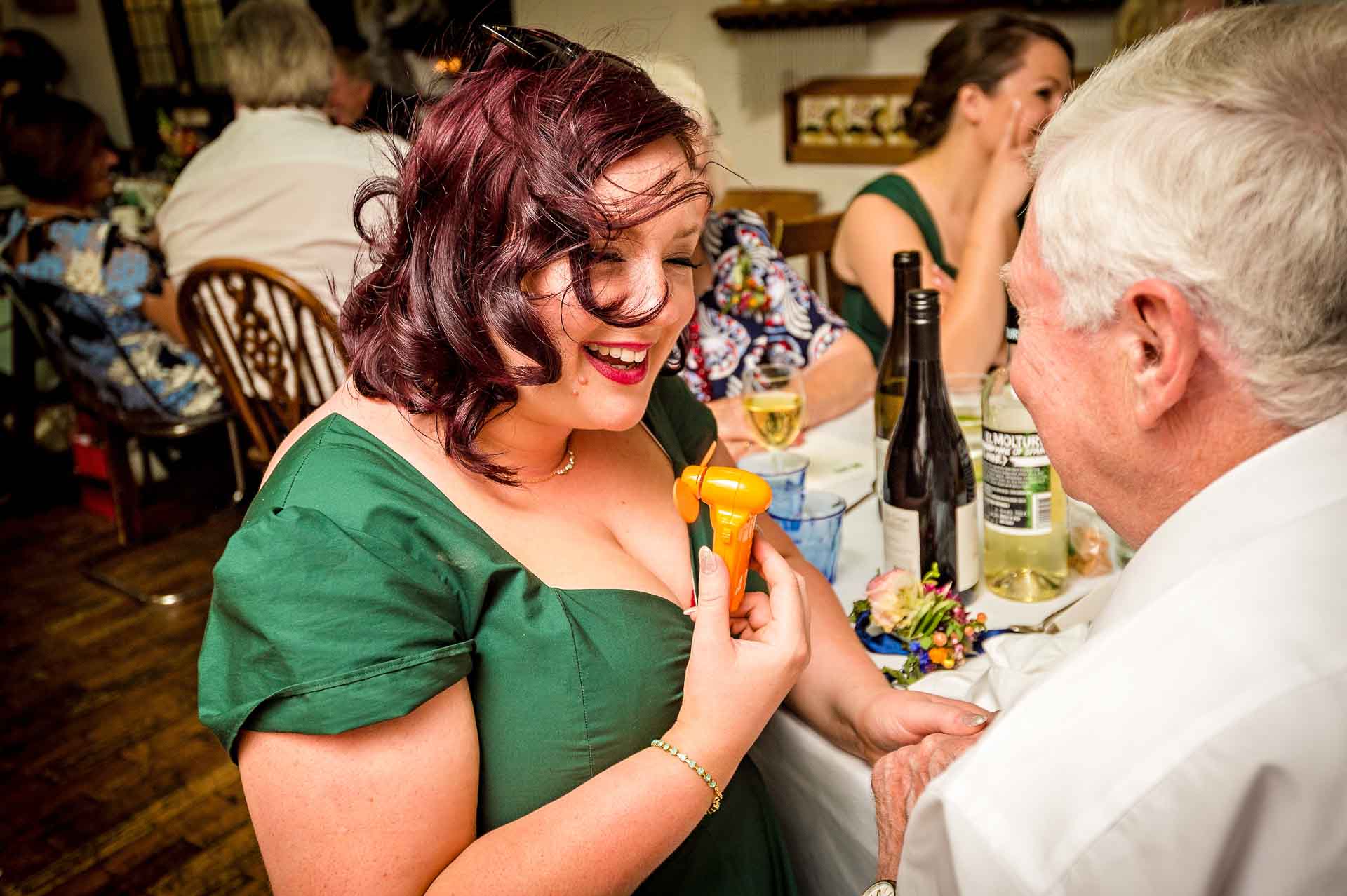 Bridesmaid at wedding meal in restaurant holding fan and laughing on a hot day