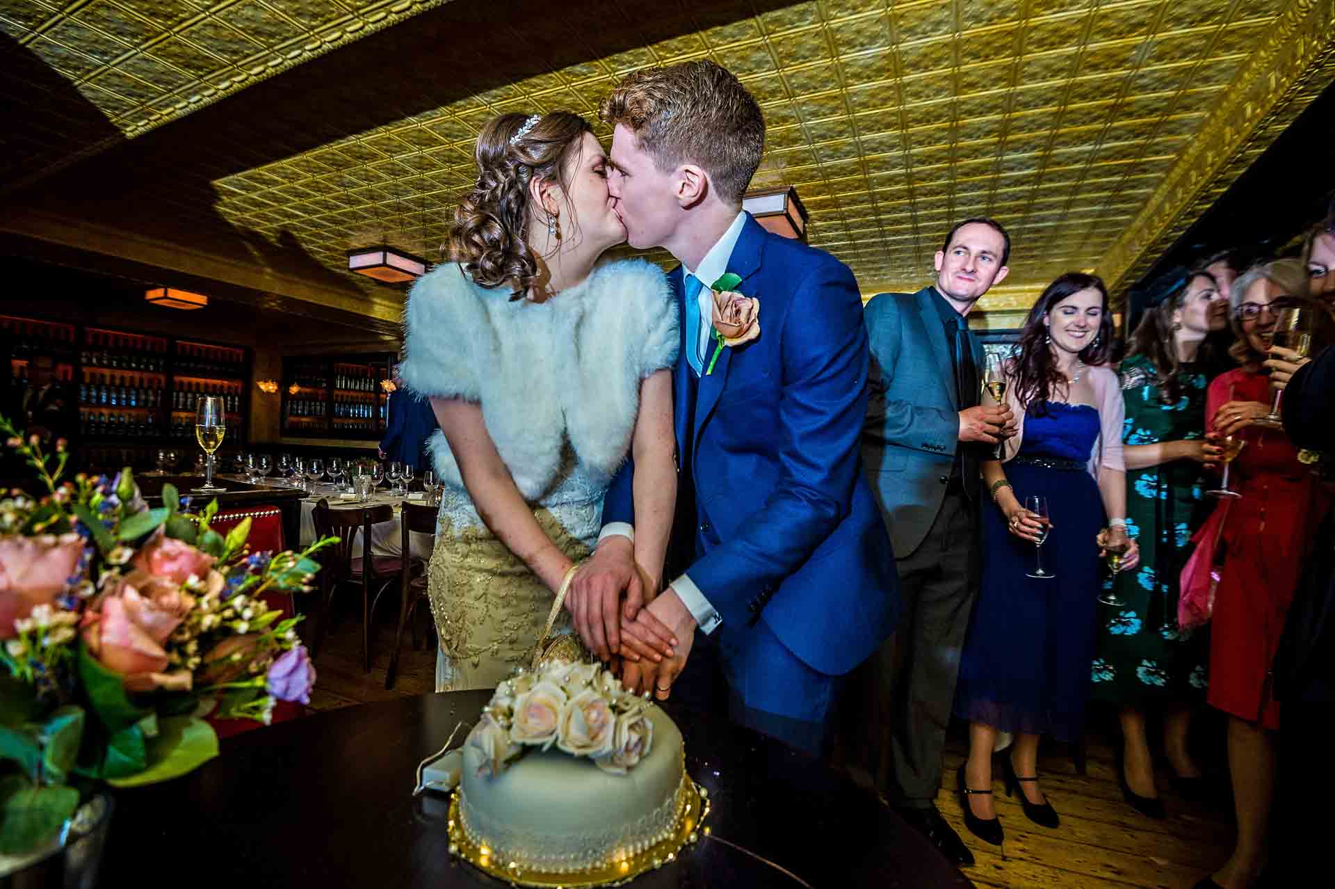 Couple kissing whilst cutting the wedding cake in Cardiff