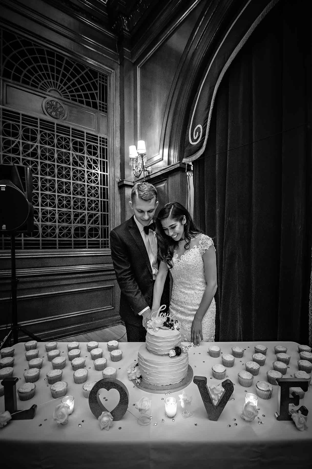 Black and white portrait of couple cutting cake behind 'Love' letters