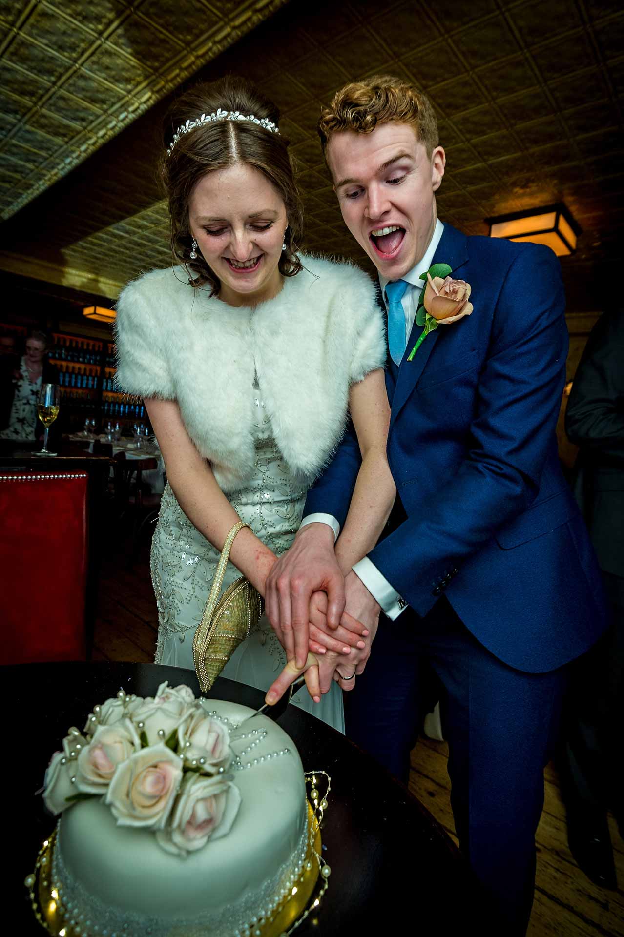 Groom looking enthusiastic as he cuts wedding cake with new wife