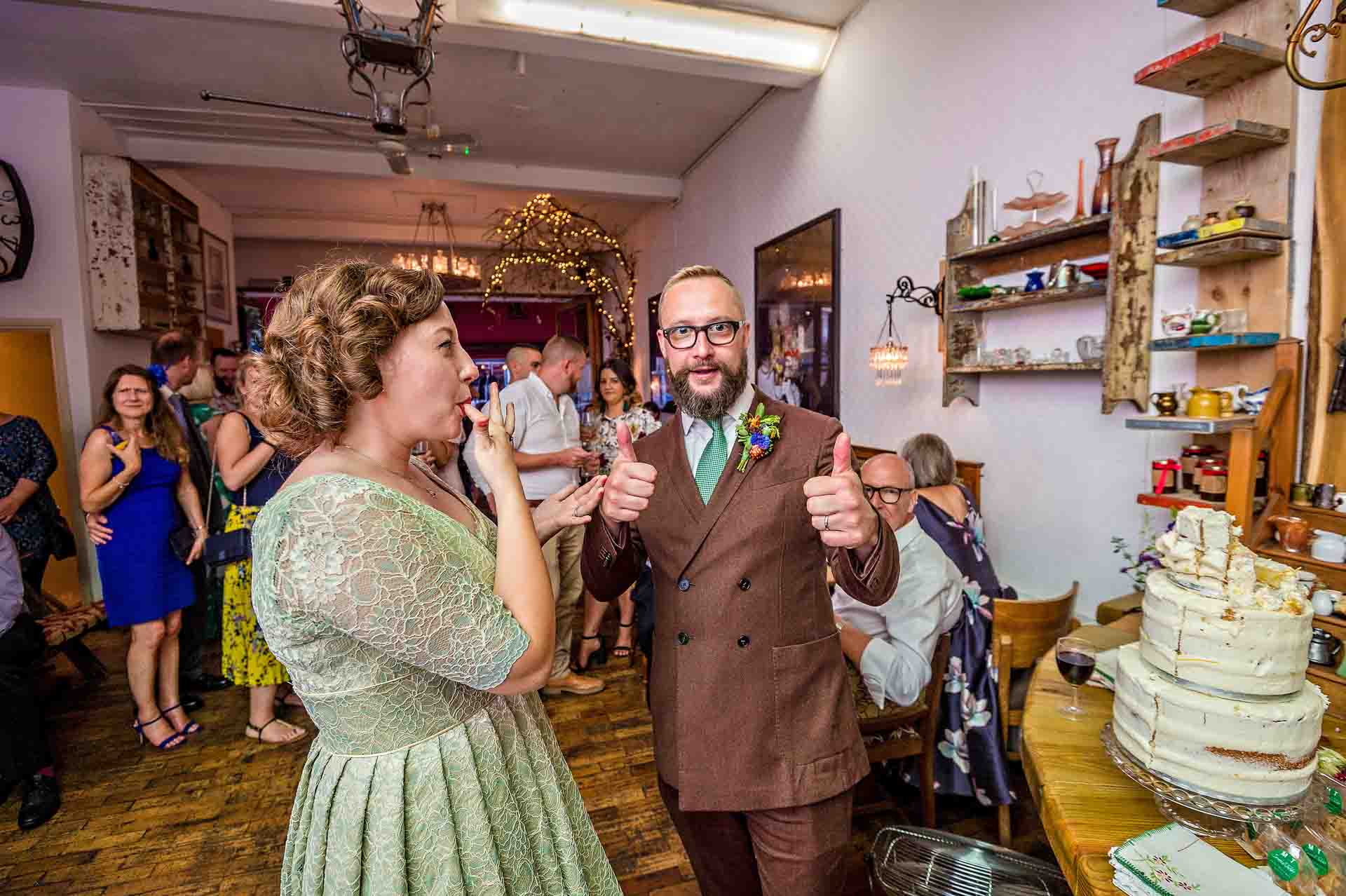 Groom giving thumbs up and bride licks fingers after the cake cutting