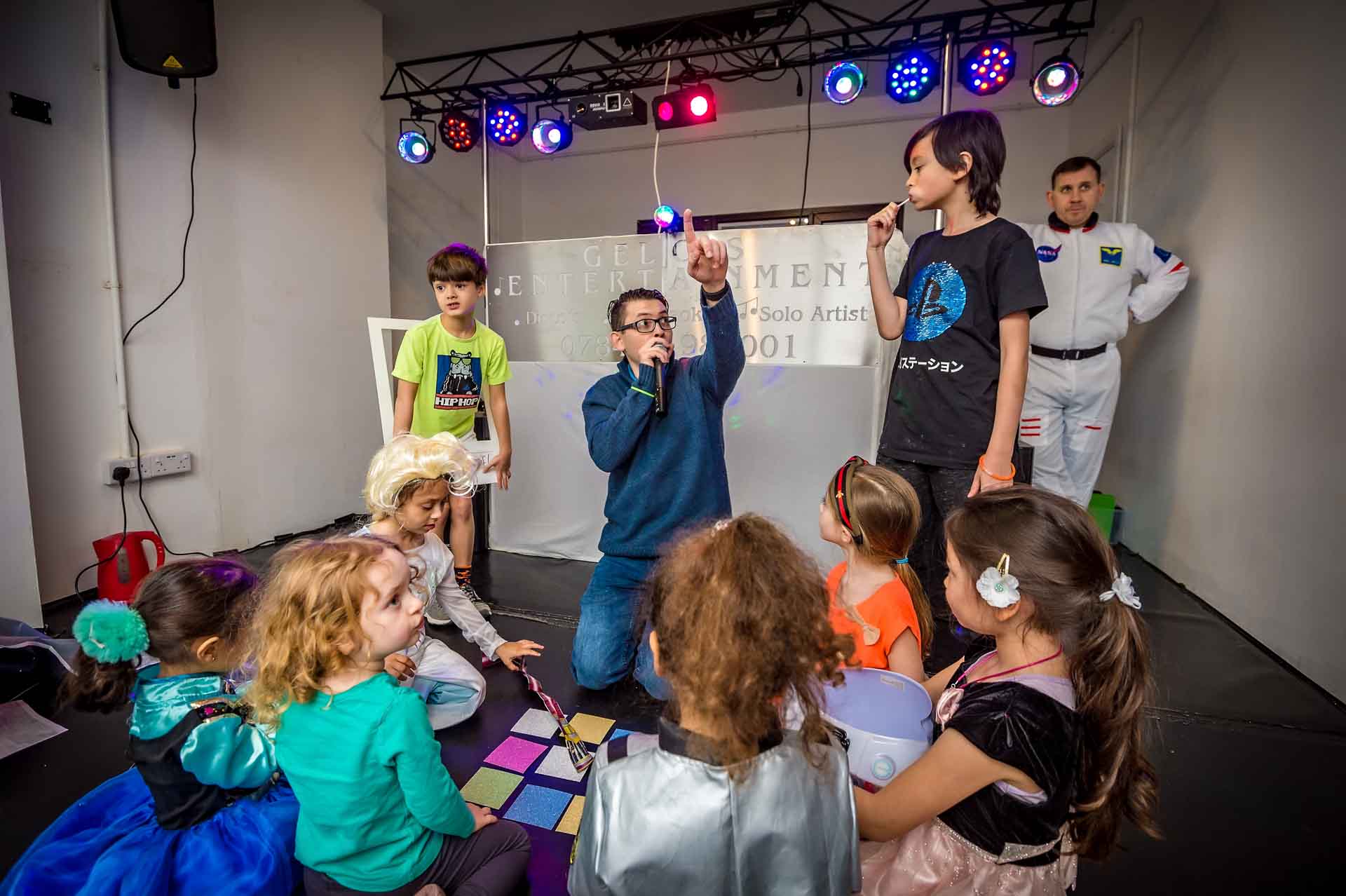 DJ pointing into air with children gathered around at birthday party