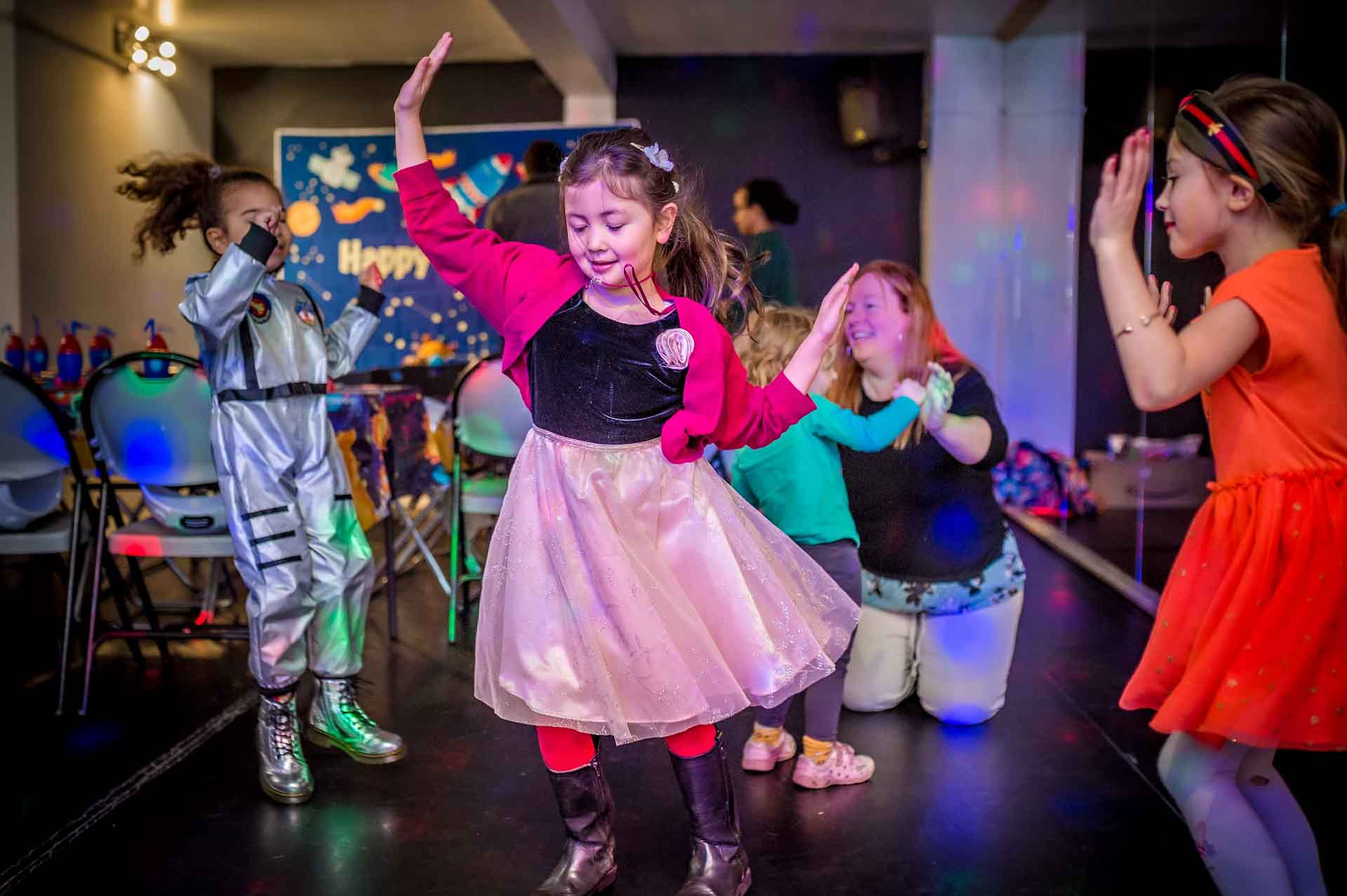 At a birthday party, children dance on dancefloor with arms in the air