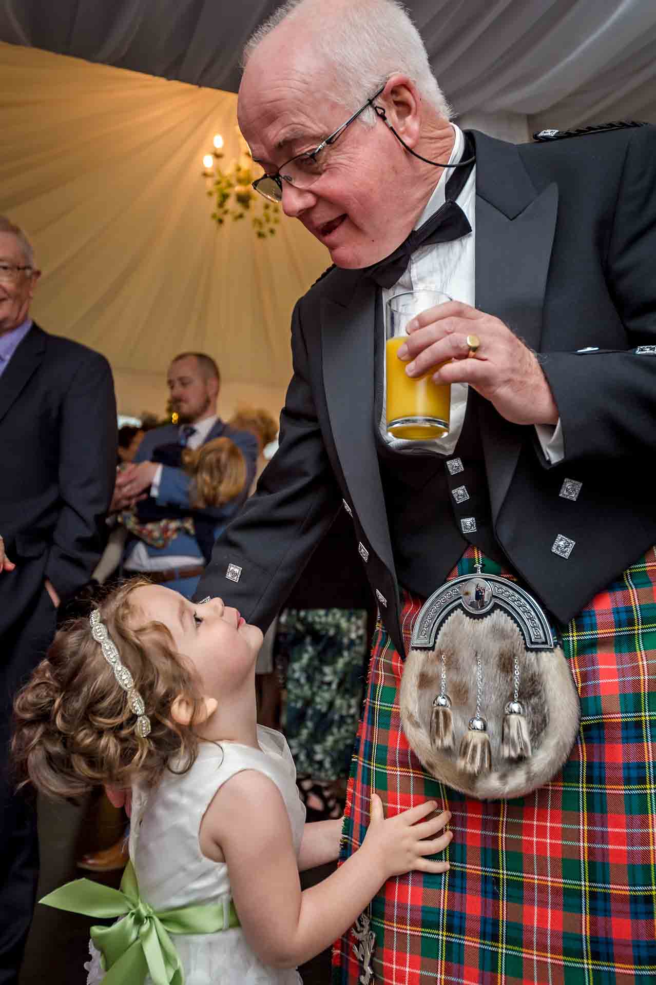 Small bridesmaid looking up at her grandfather in kilt at Llechwen Hall Hotel wedding reception