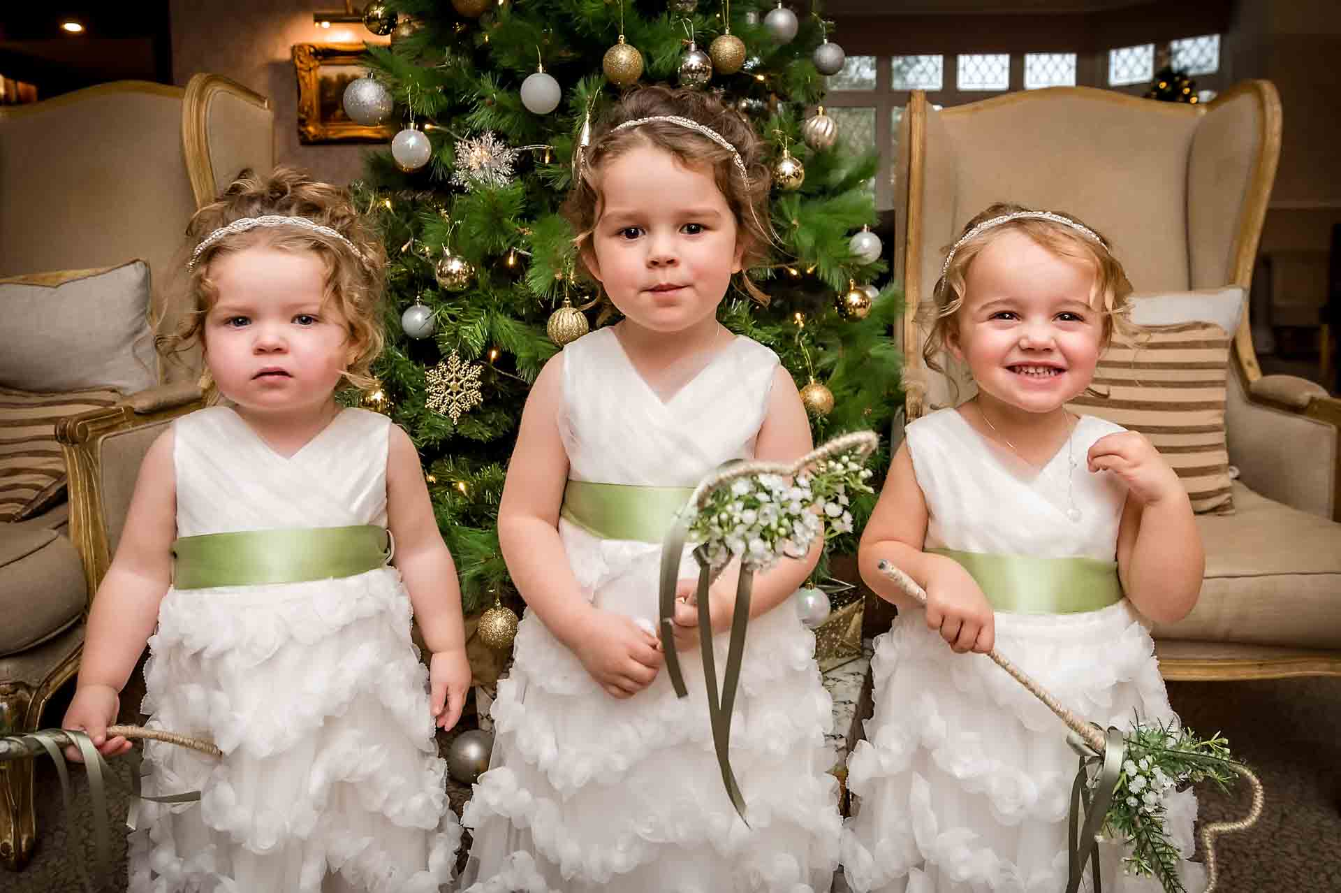 Three toddler bridesmaids standing in front of Christmas tree at Llechwen Hall Hotel wedding