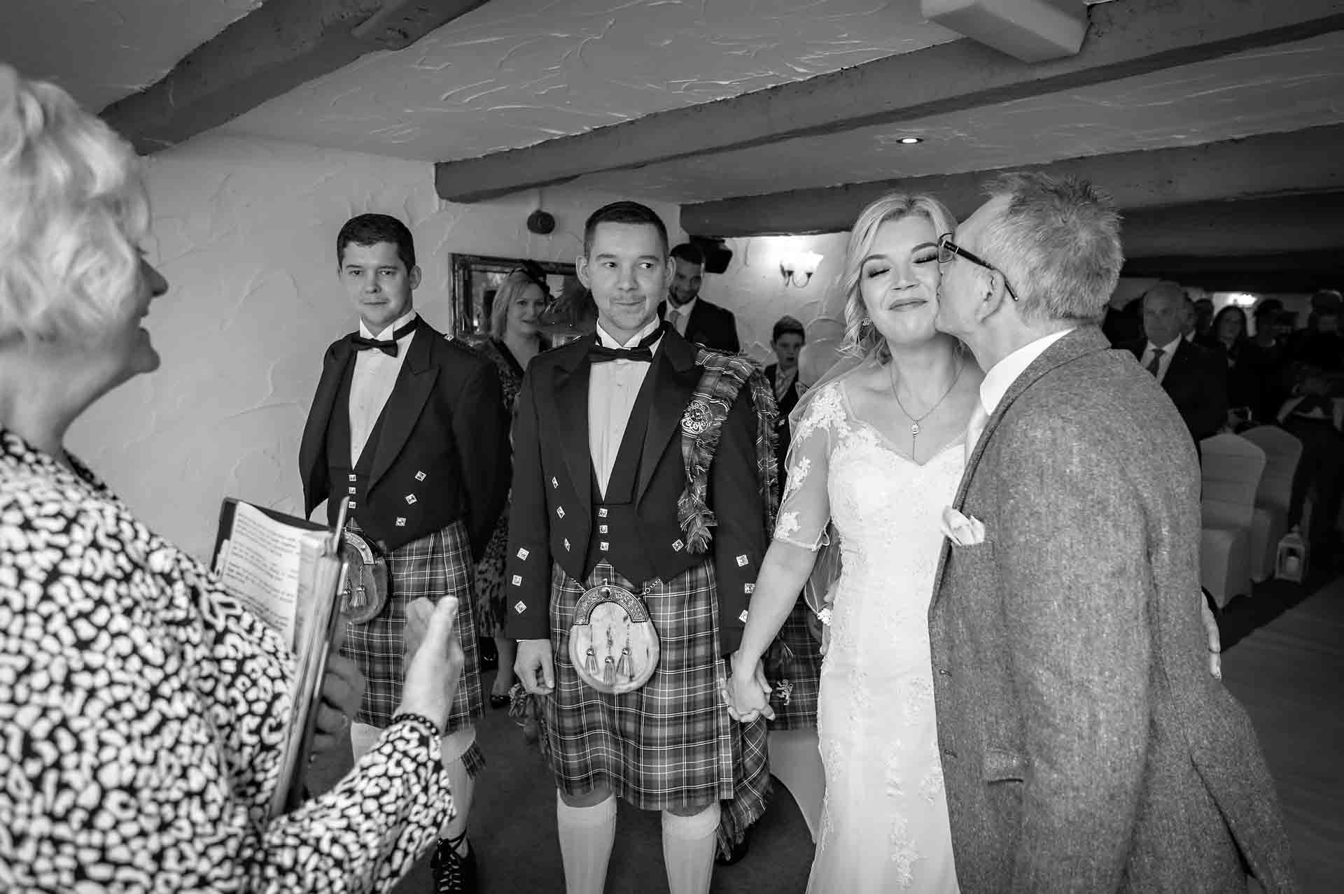 The father of the bride kisses her on cheek at start of the wedding ceremony