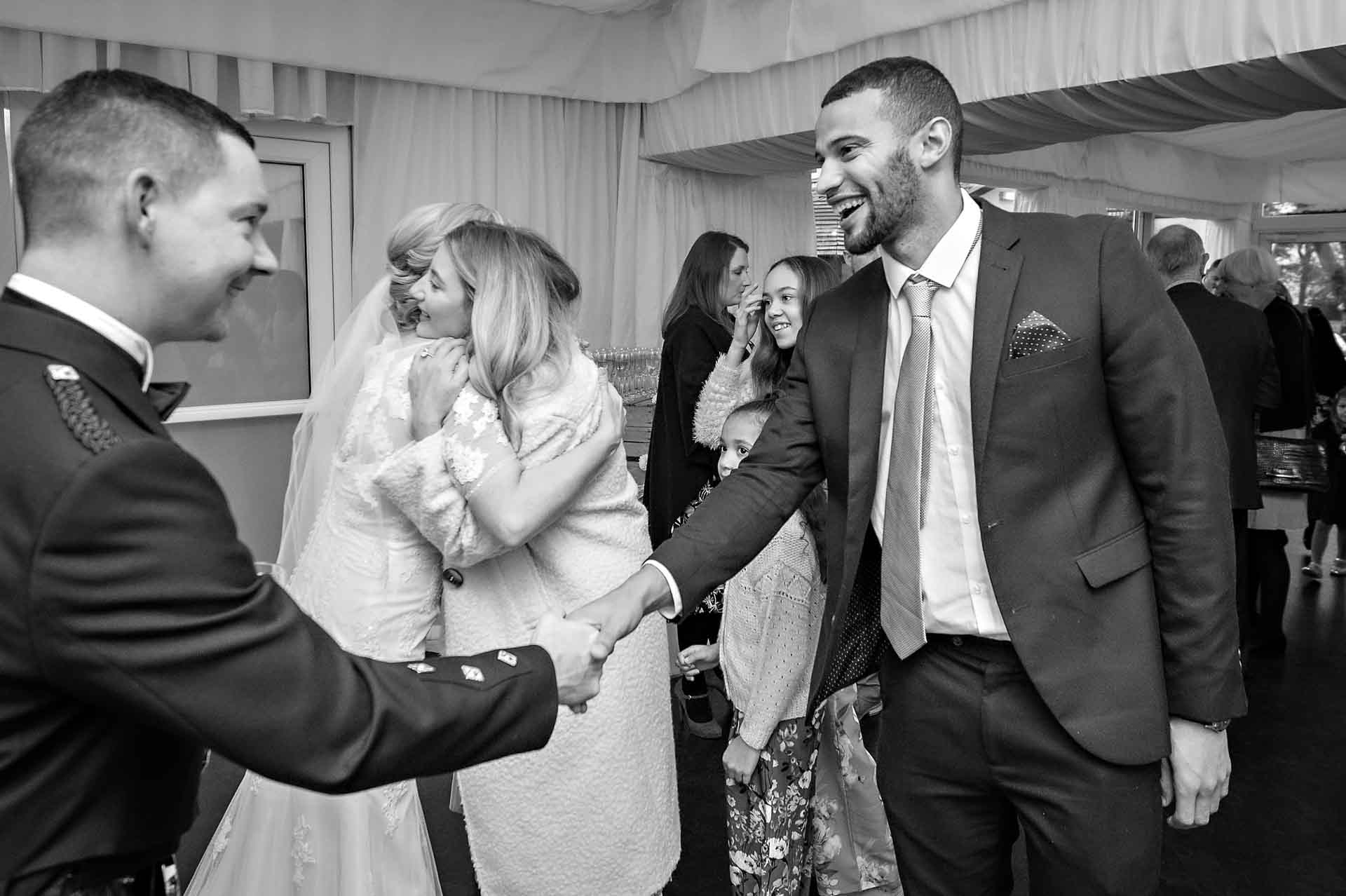 Groom shakes hands with male guest with bride being congratulated in background