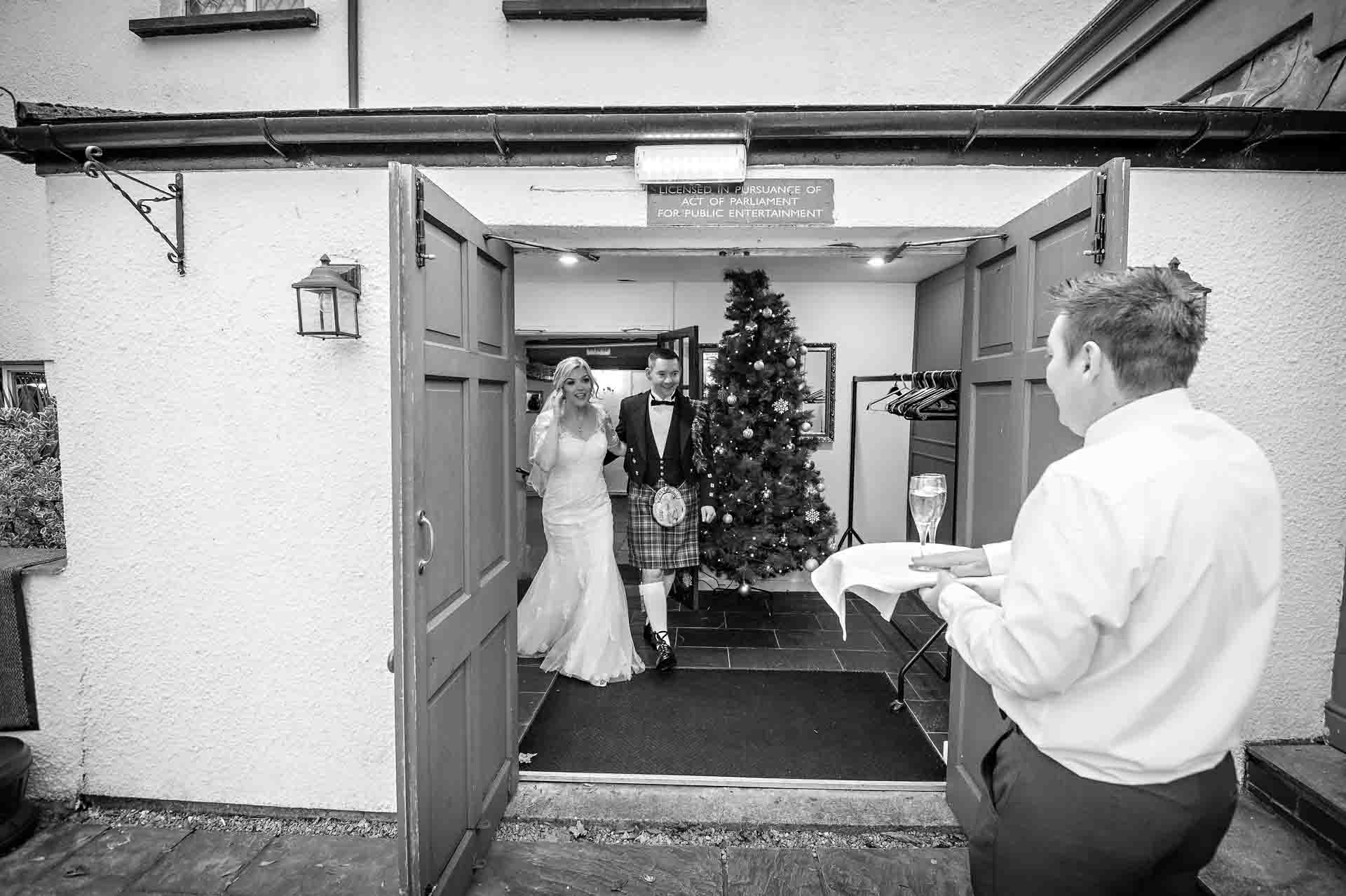 A waiter waits with drinks as the couple leave the Nelson Suite at their Llechwen Hall Hotel wedding
