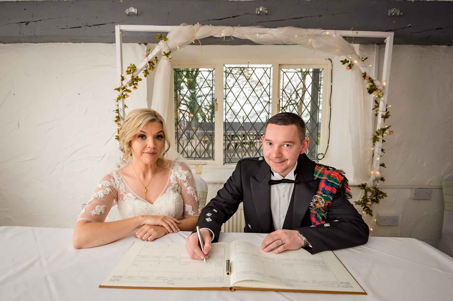 The groom pretends to sign the 'dummy' register at Llechwen Hall Hotel whilst the bride watches on