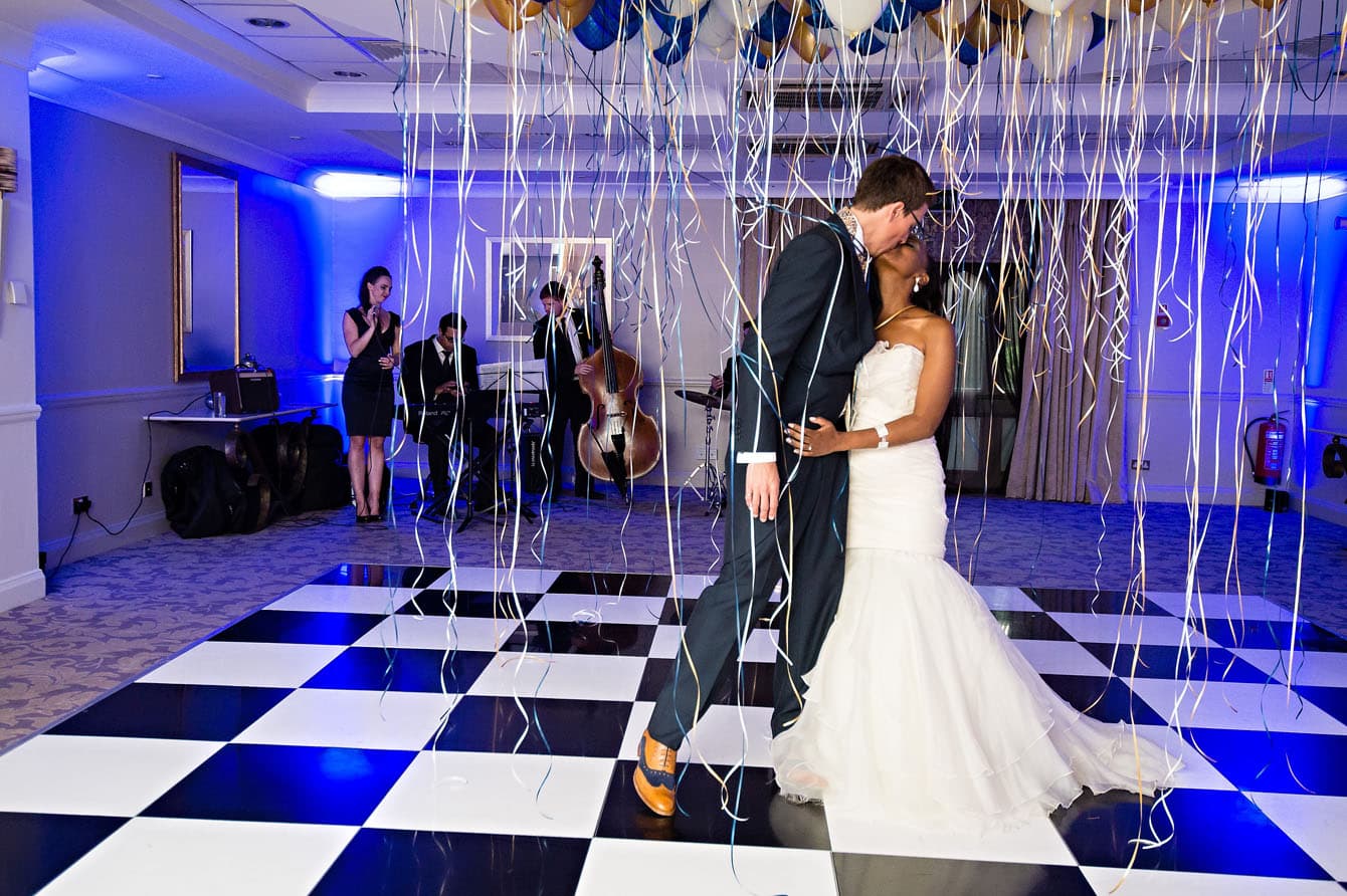 Bride and Groom kissing whilst dancing under streamers from balloons