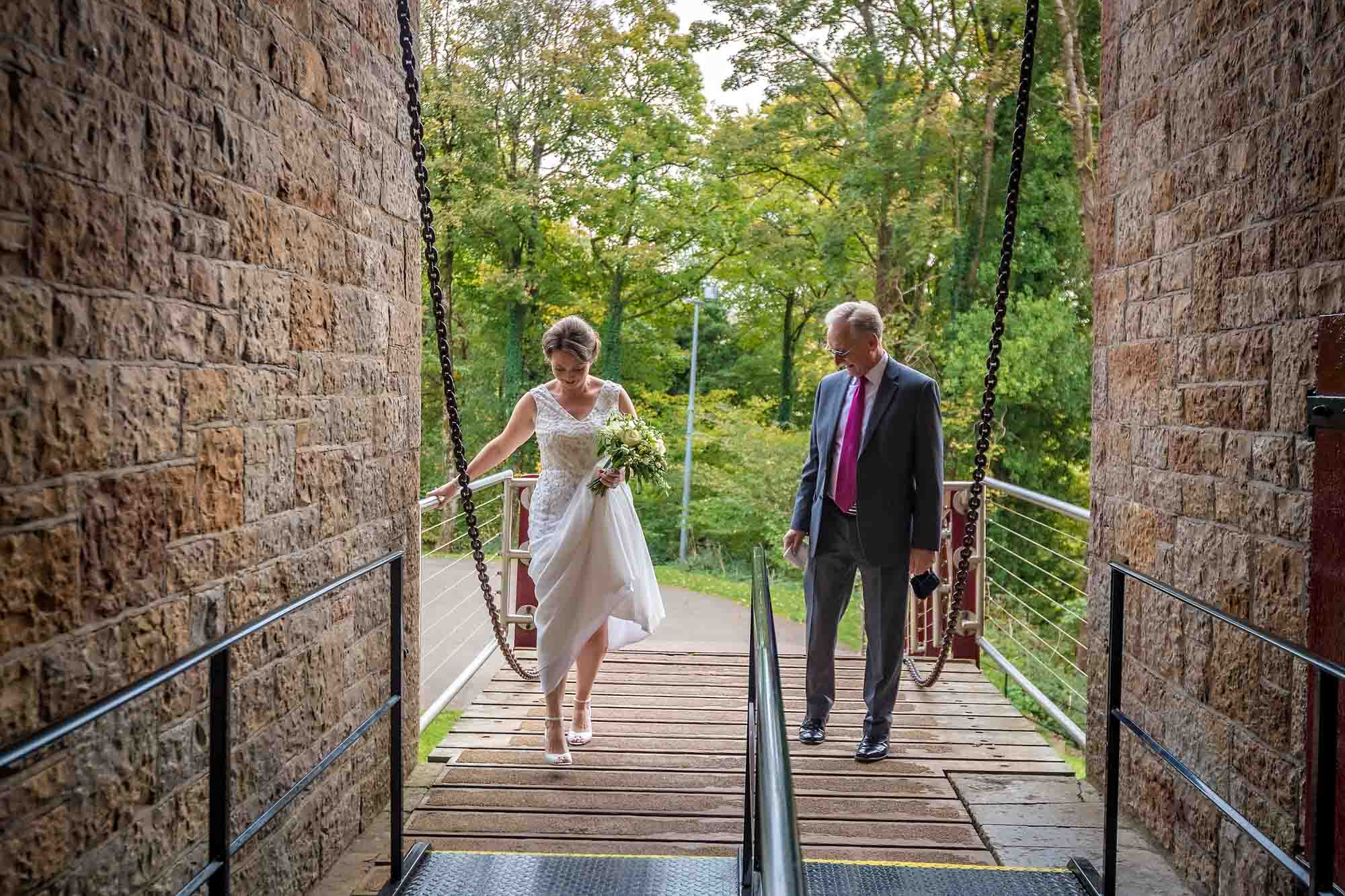 The bride's father admires her as they cross the drawbridge at Castell Coch