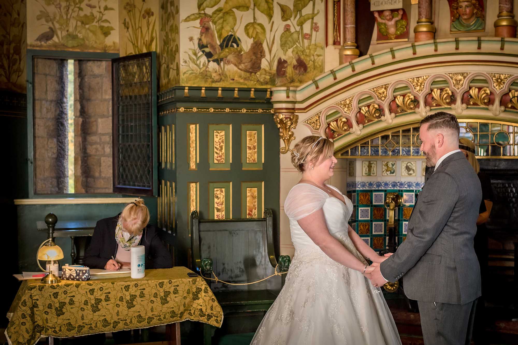 Couple holding hands in the Drawing Room at Castell Coch with a masked register writing at table