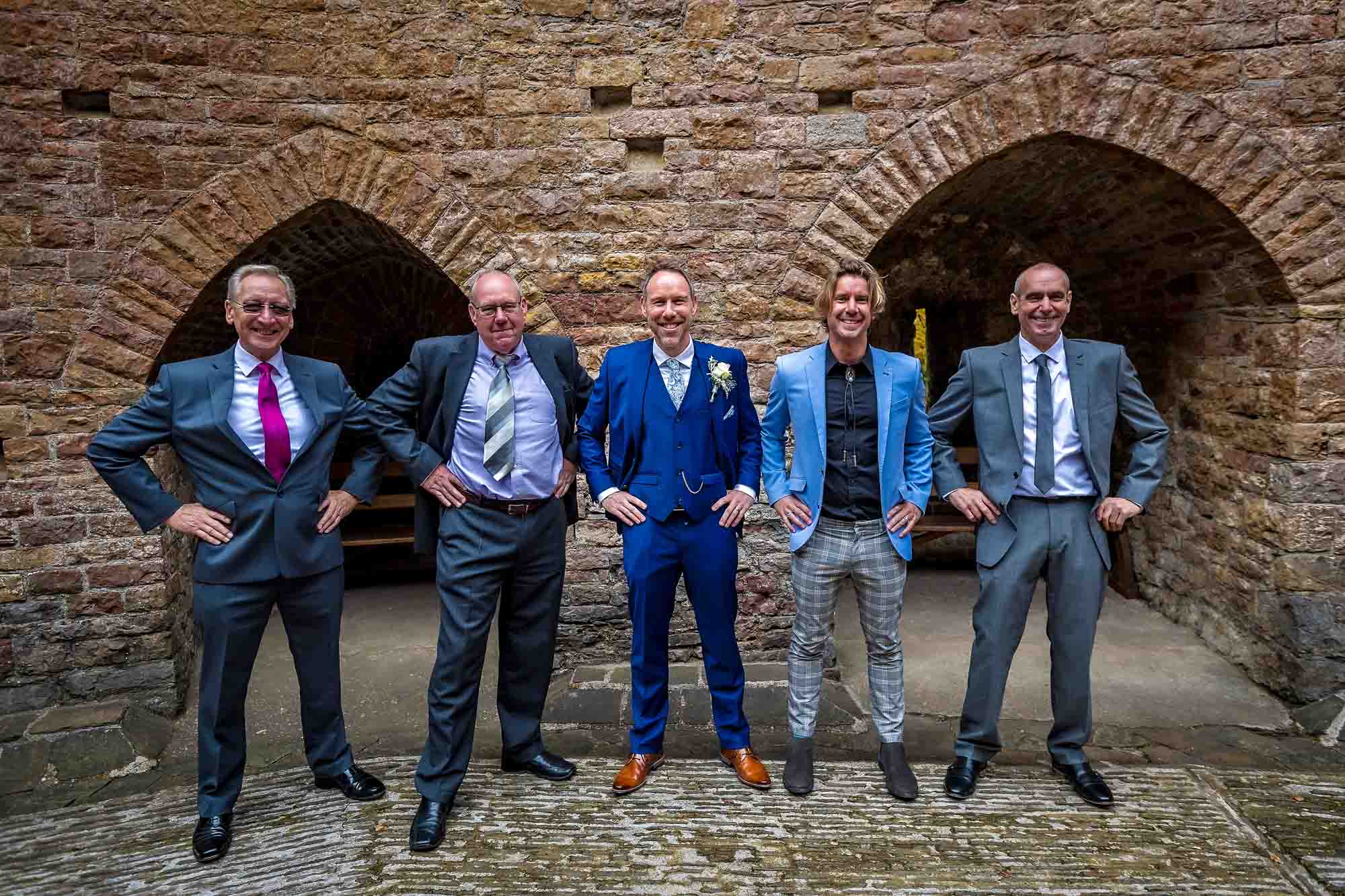 Groom poses in quirky images with four male guests with hands on their hips at Castell Coch