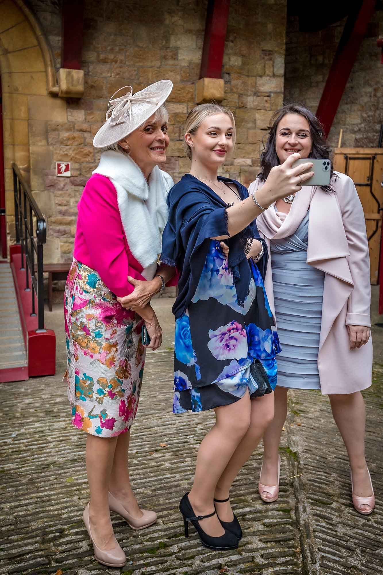 Three female wedding guests taking a selfie in the courtyard of Castell Coch