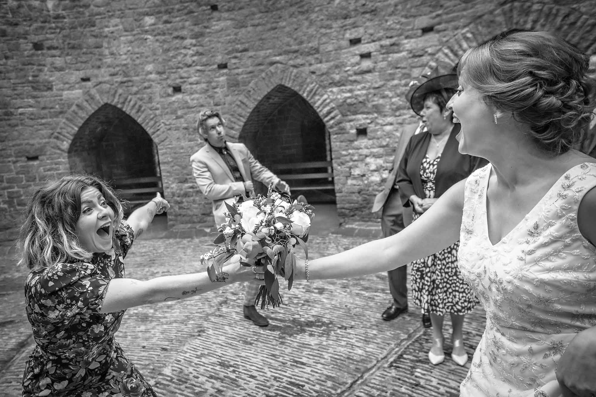 The bride hands the bouquet to a friend who is pointing at her partner as he runs off