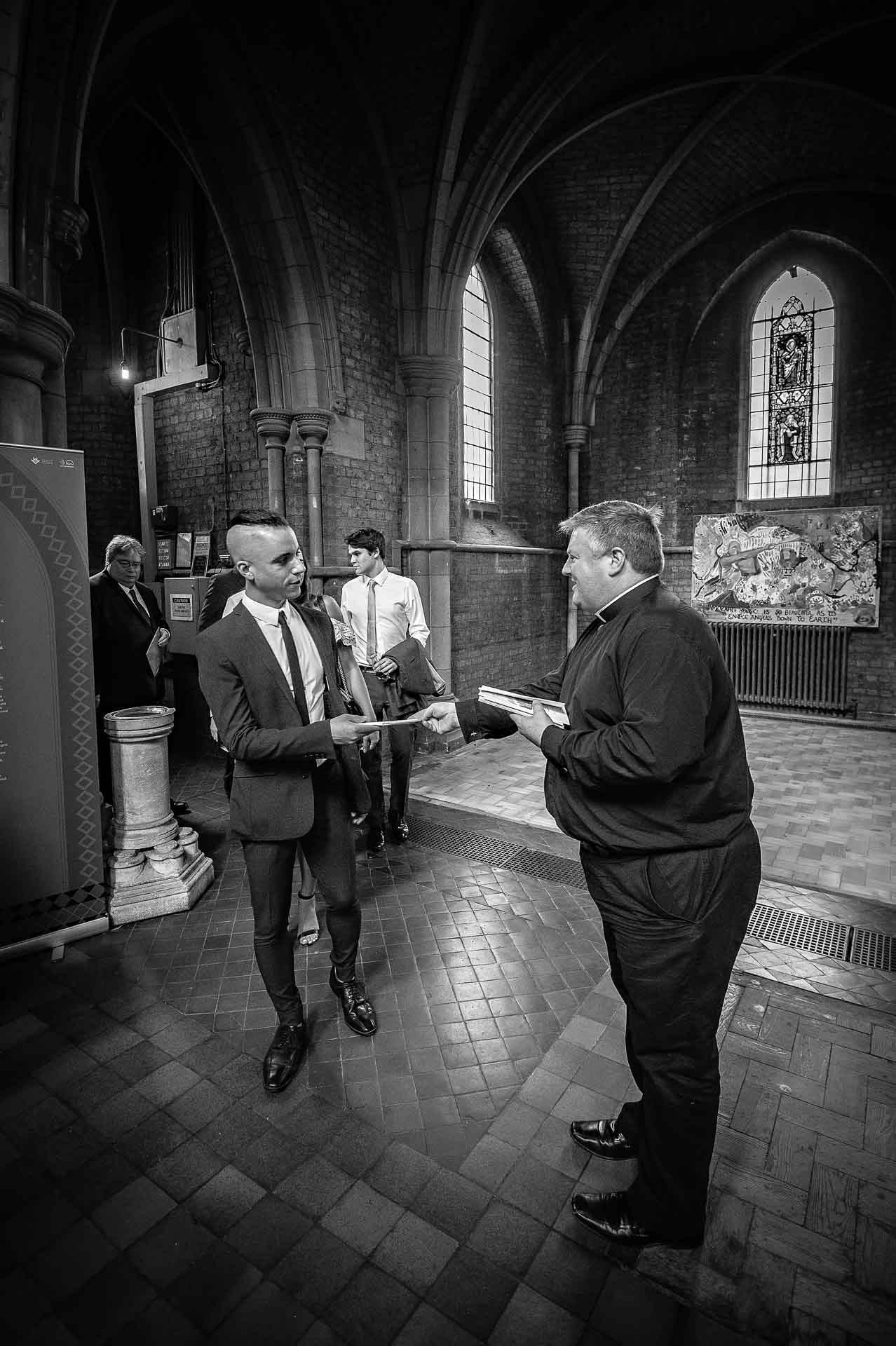 Vicar giving out order of service to guest at a wedding