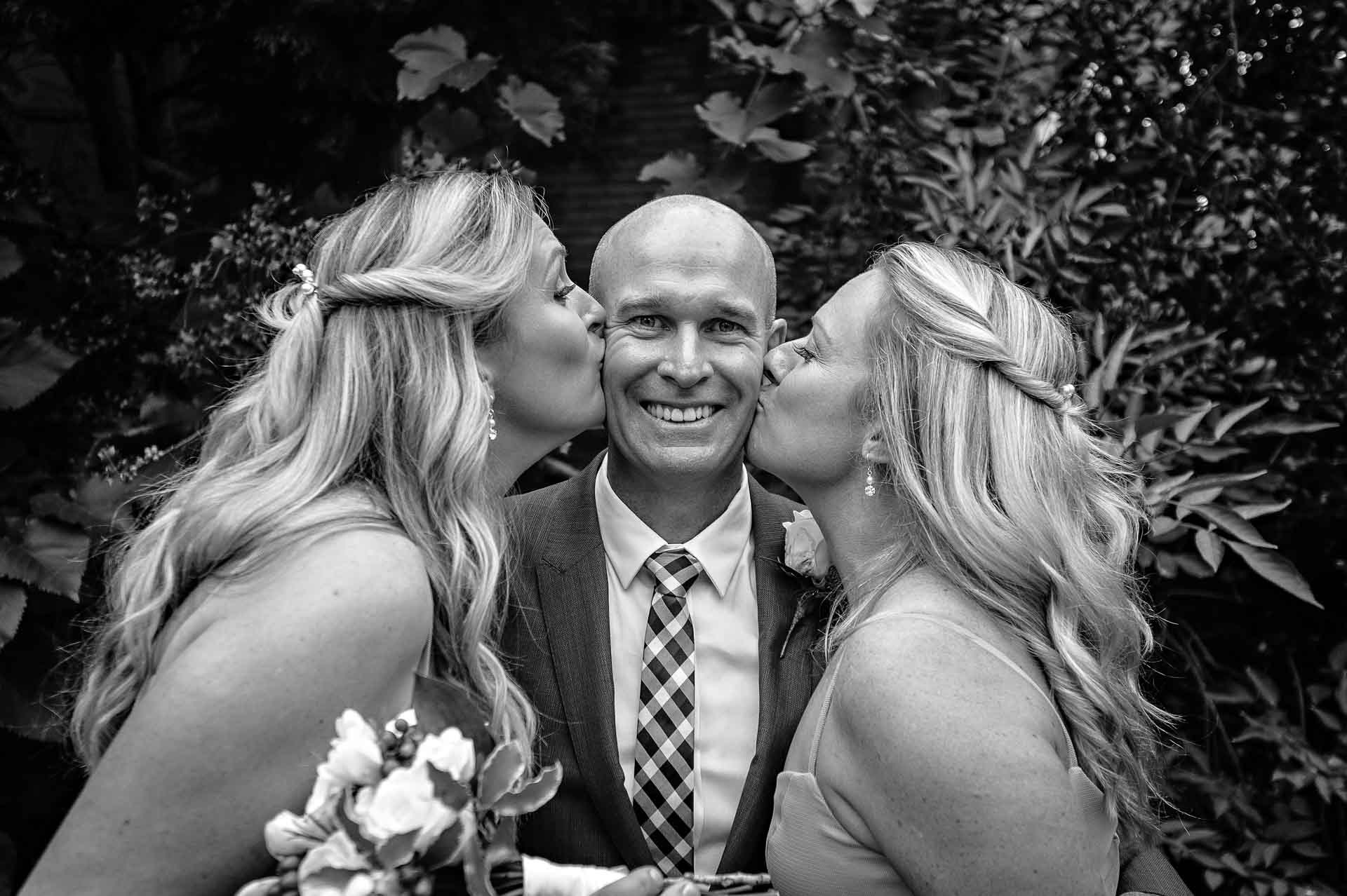 Two bridesmaids kissing groom on cheeks in black and white
