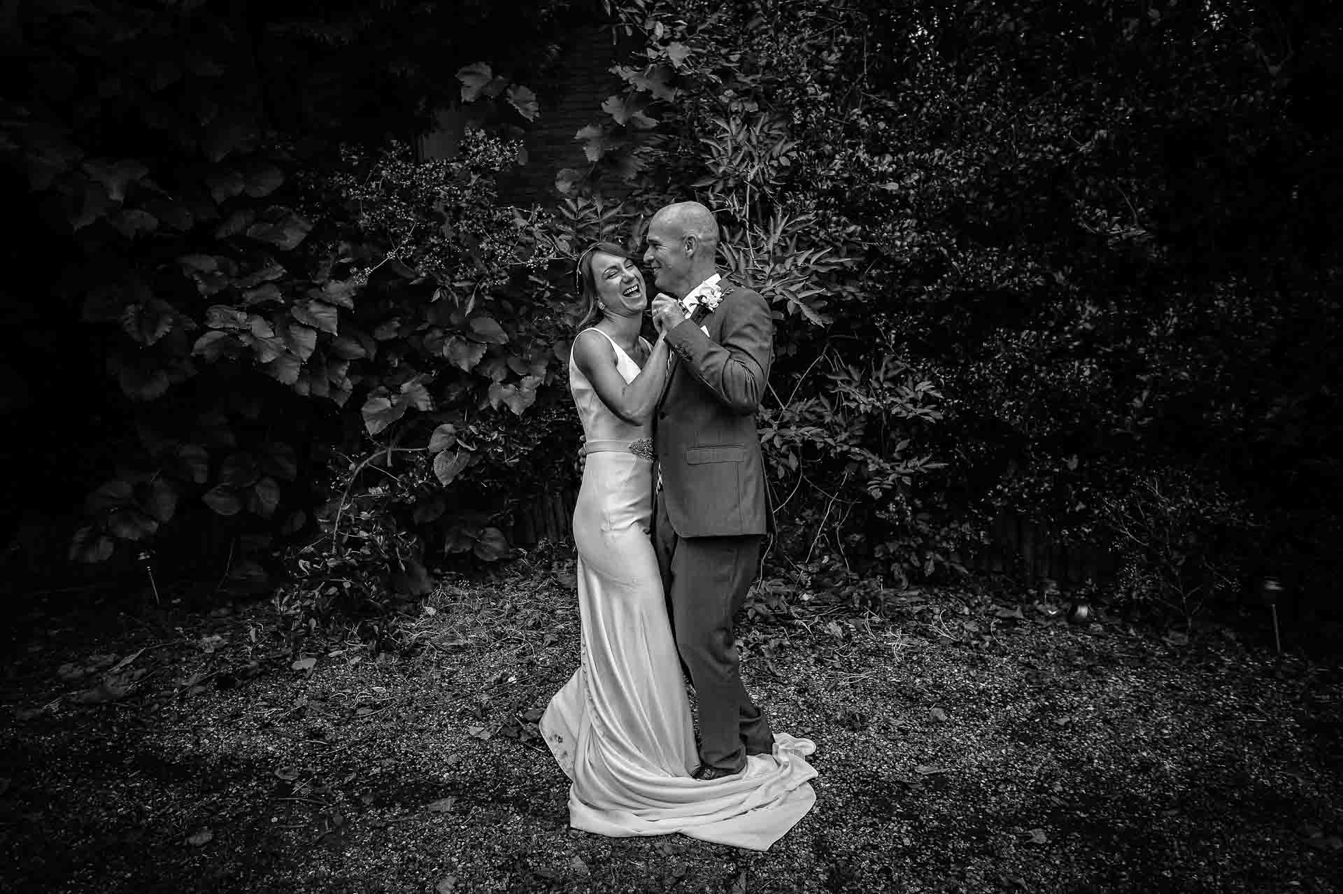 Newly-weds in garden dancing with each other in black and white