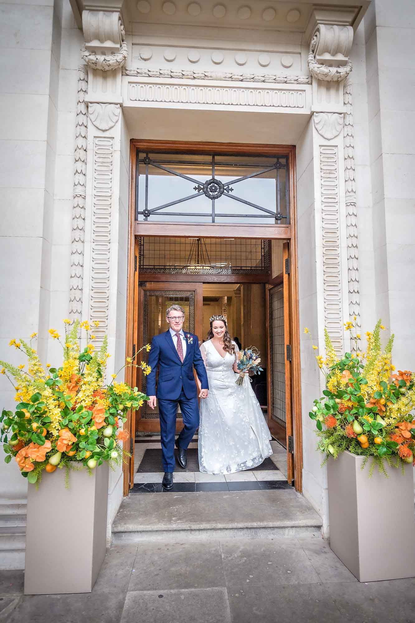 A beaming bride and groom exit the Old Marylebone Town Hall after their wedding ceremony