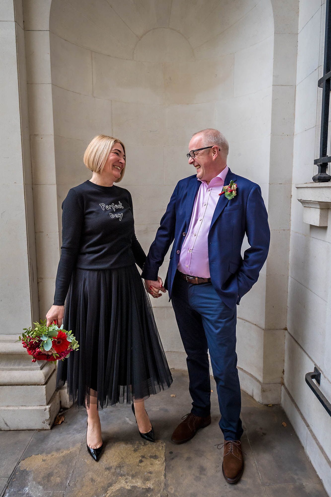 Wedding couple holding hands and smiling at each other in alcove outside the London Business School, Marylebone