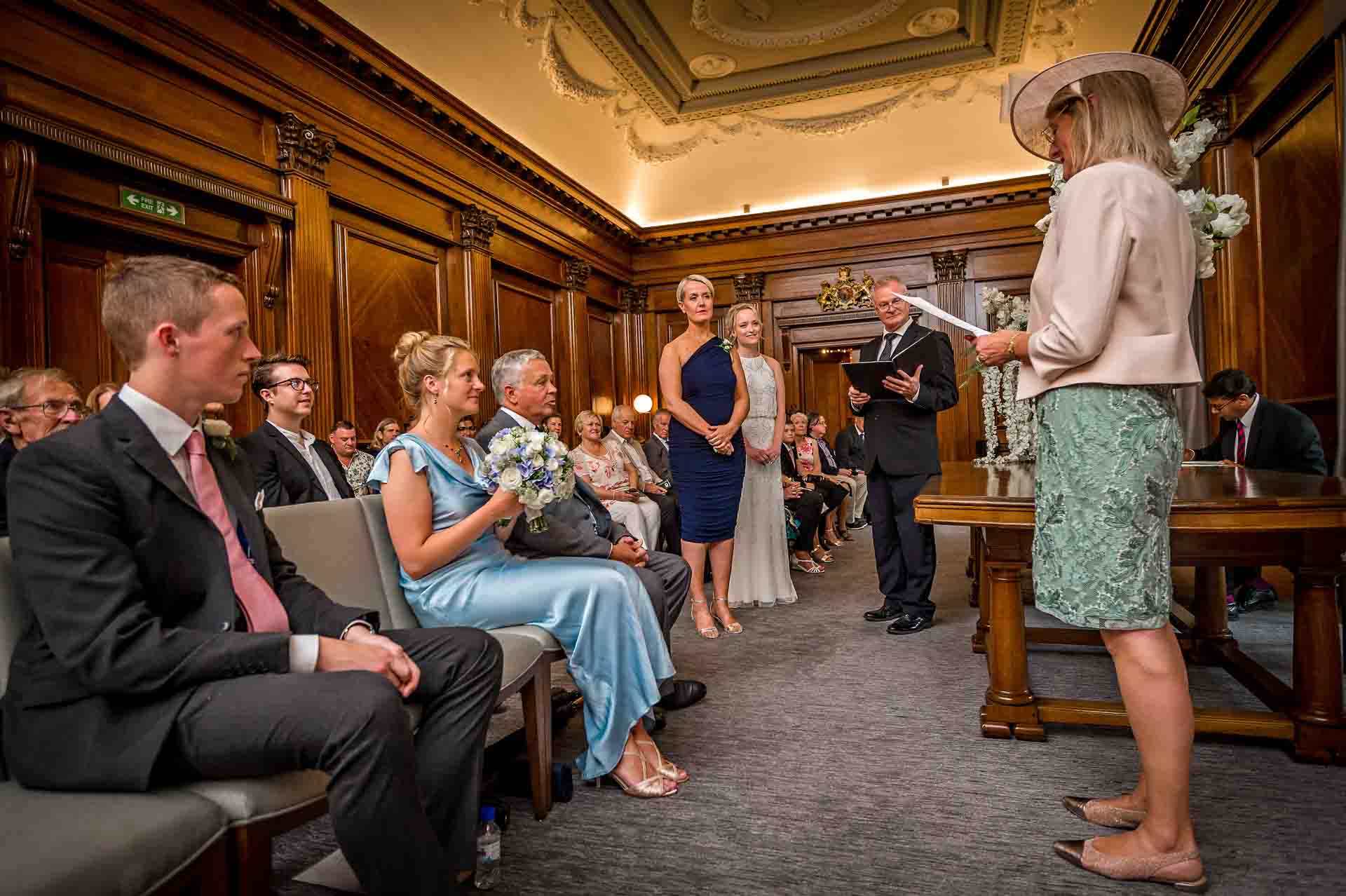 Female relative gives wedding reading at Marylebone Town Hall with brides and guests watching