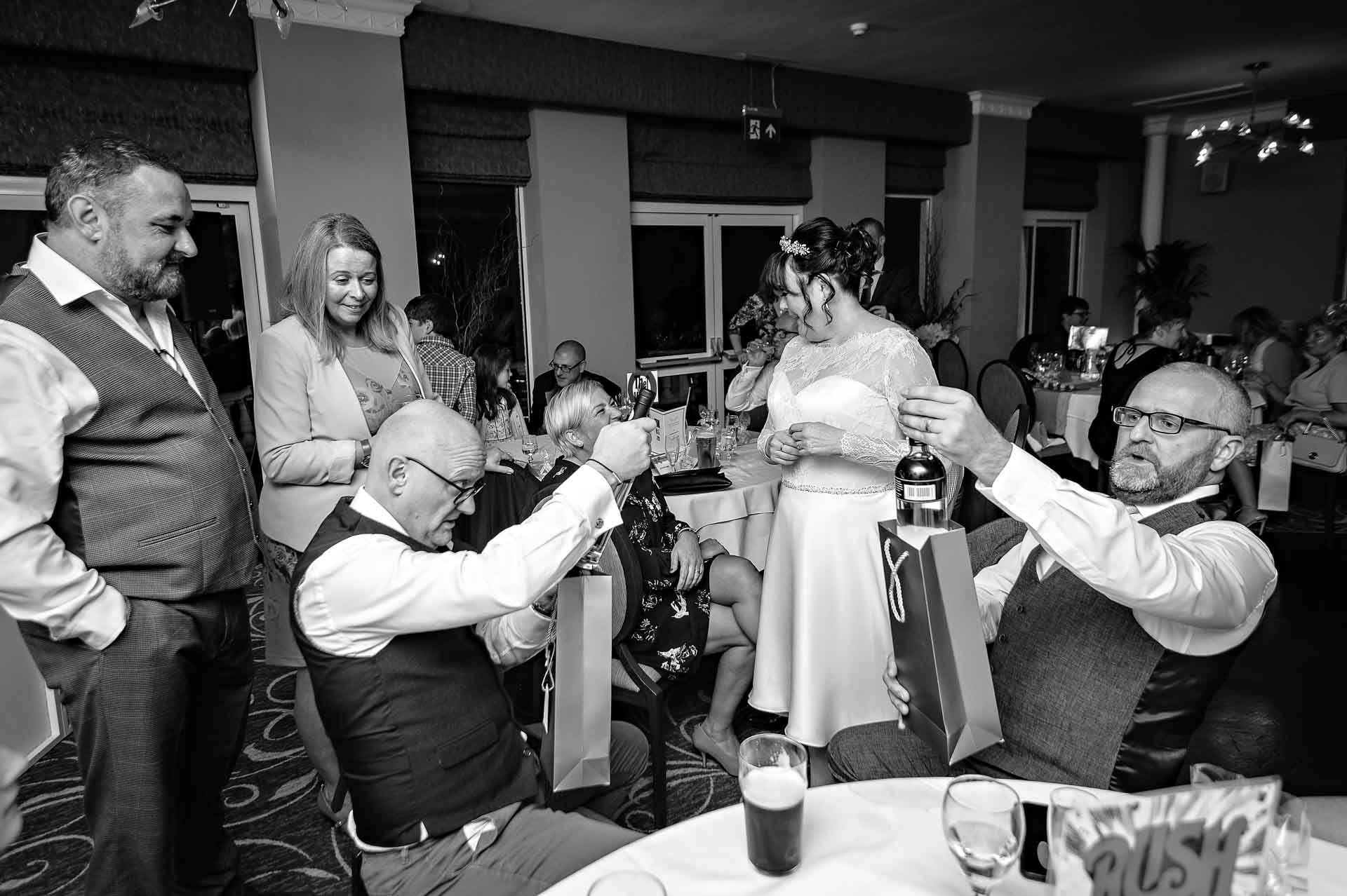 Two Men at Wedding Looking at Bottles of Wine with Bride and Groom Watching - Black and White