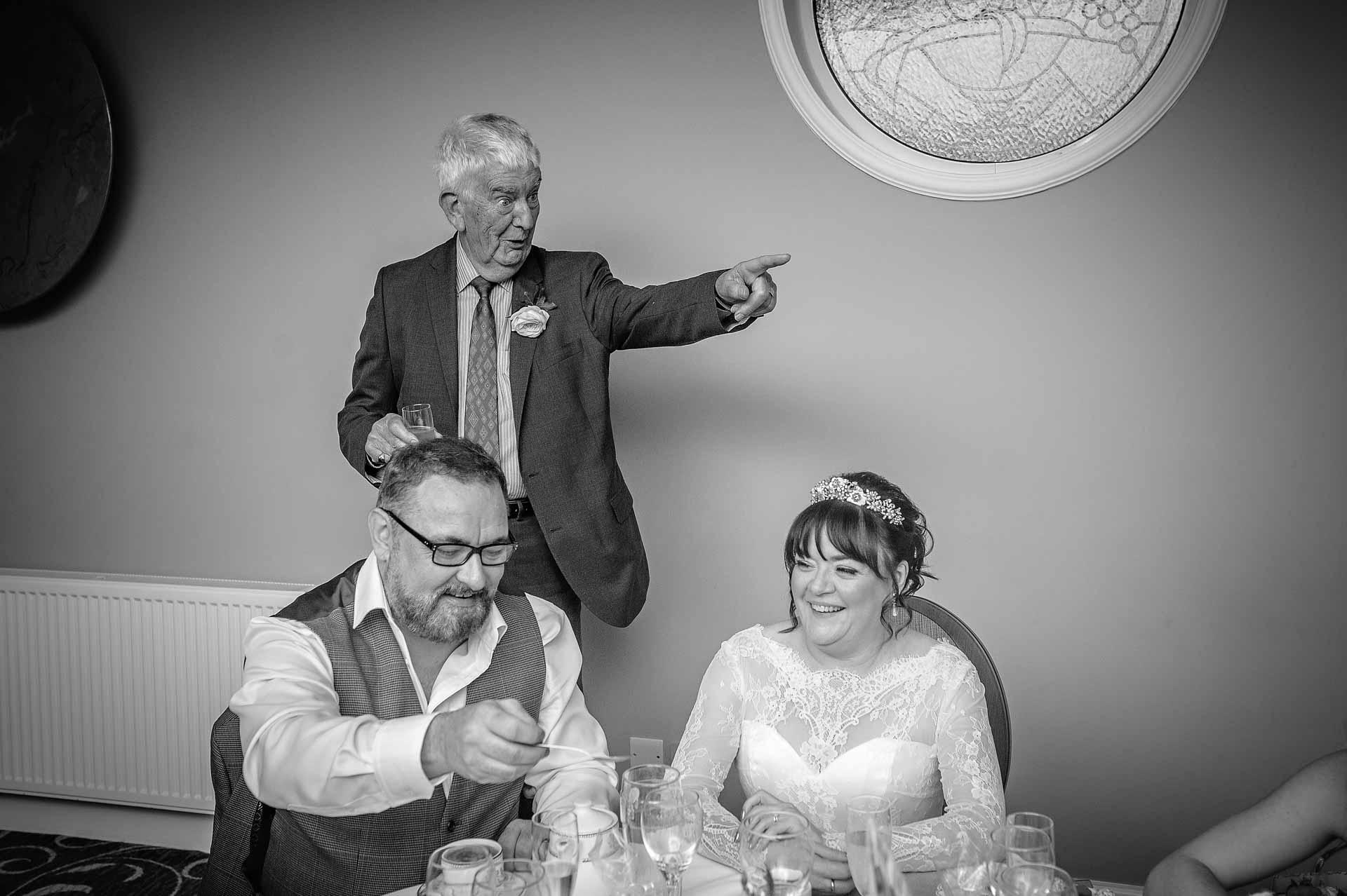 Bride's father pointing during speeches whilst the couple laugh