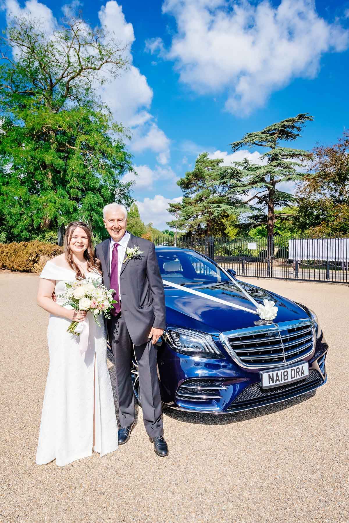Bride and father posing with Mercedes wedding car in the sunshine outside Danson House.