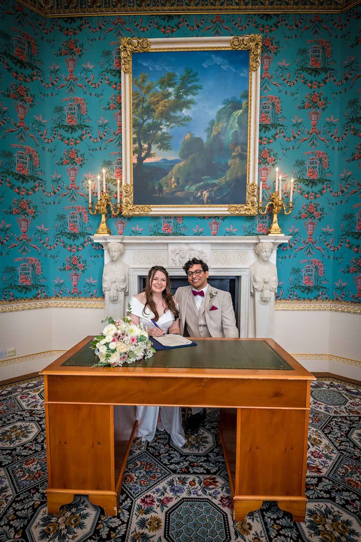 A newlywed couple pose with the wedding register in the Salon at Danson House