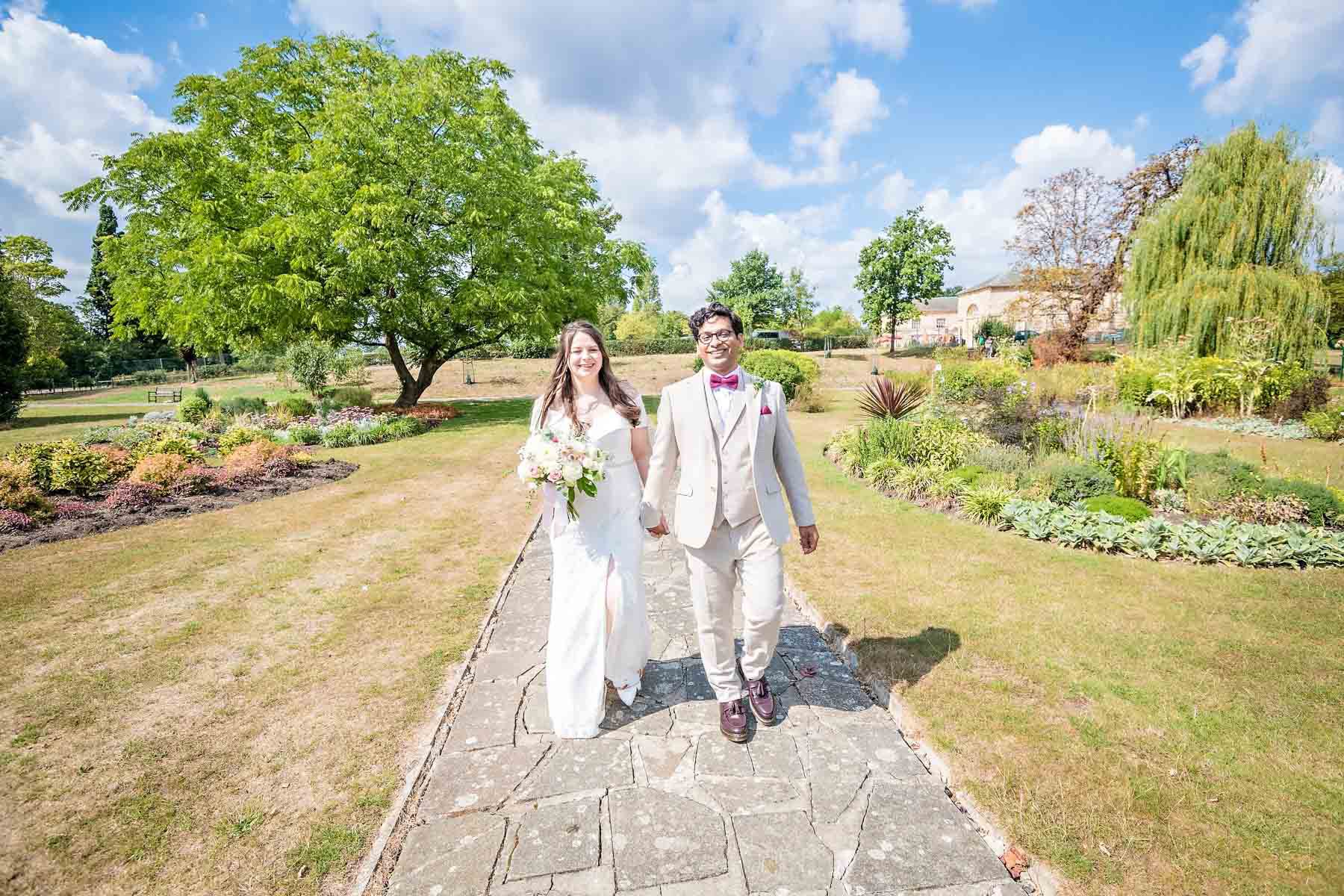 Wedding couple holding hands and walking through Danson Park in Bexley