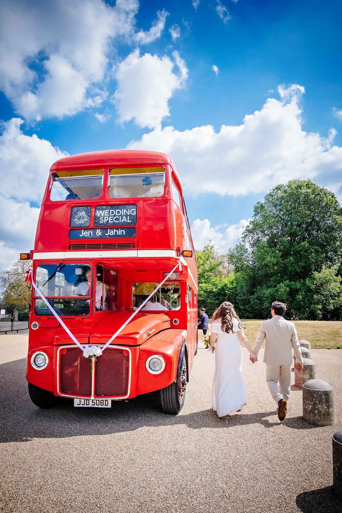 Couple holding hands and walking away towards red wedding Routmaster bus