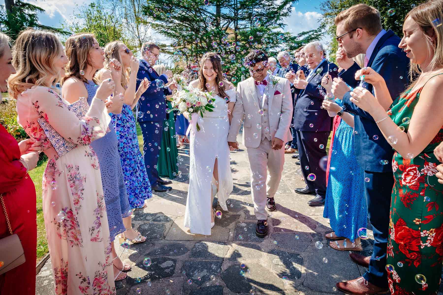 Wedding couple walking through aisle of guests blowing bubbles in Danson Park