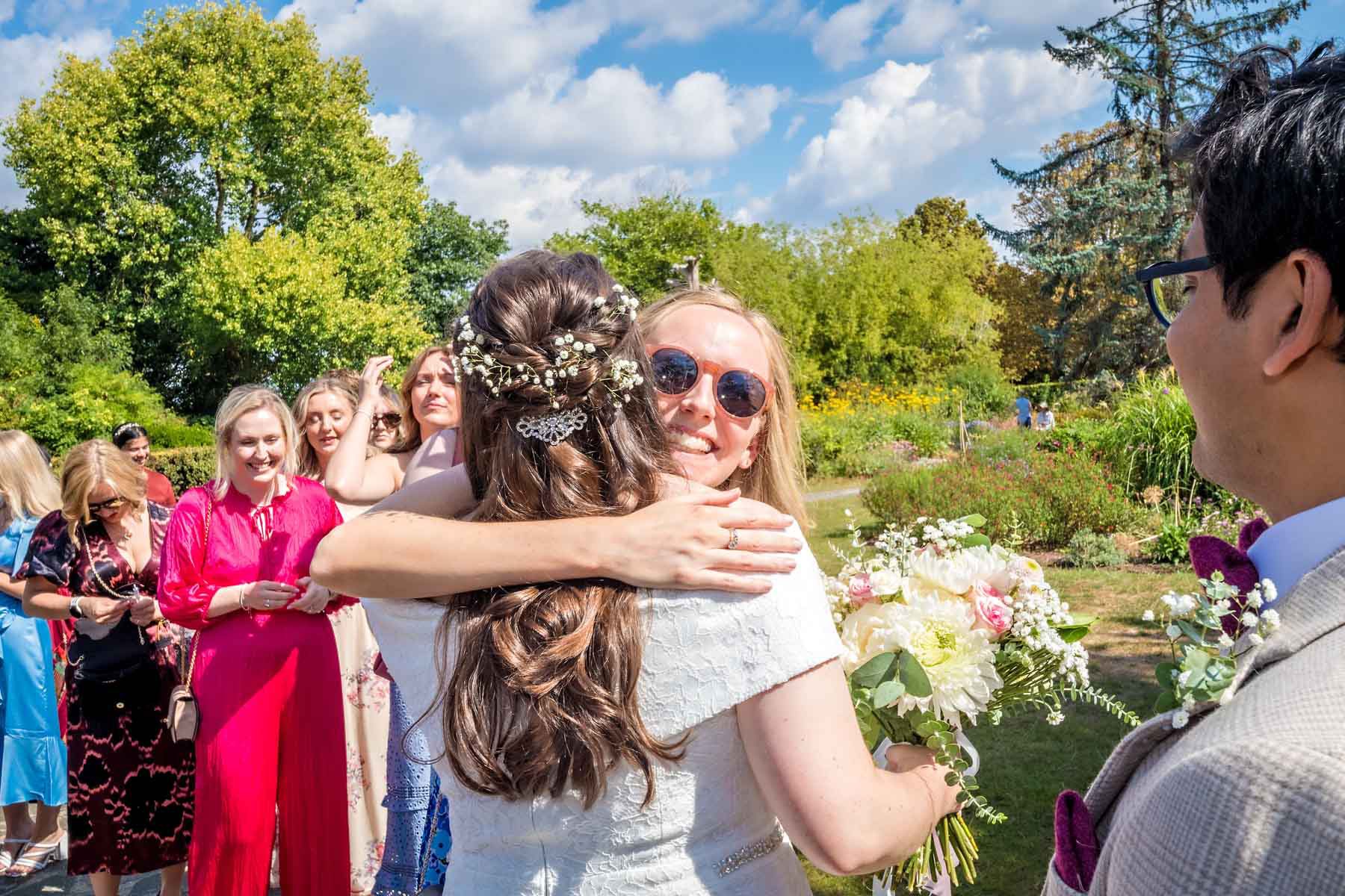 A female guest greets the bride with a hug as the groom looks on