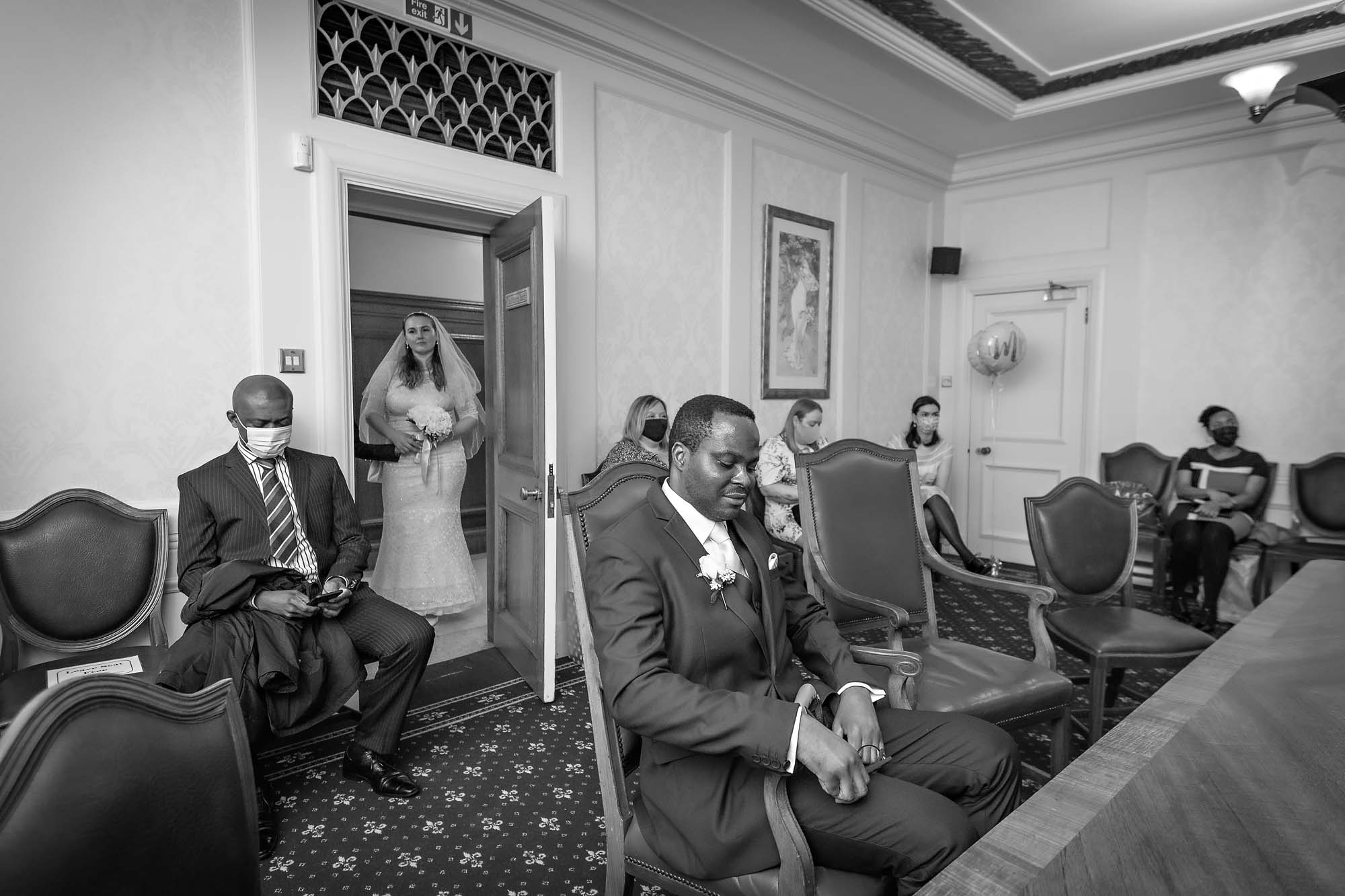 A pensive groom seated as his bride enters the Victoria Room at Wandsworth Town Hall