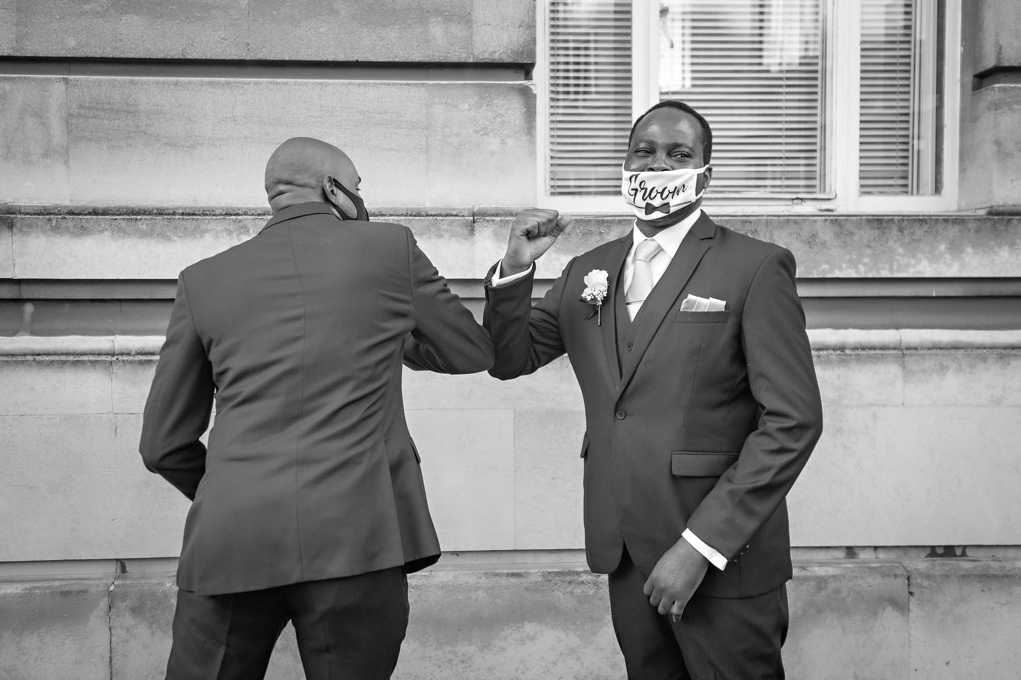 A masked groom elbow bumps a friend at his Cov-19 restricted wedding