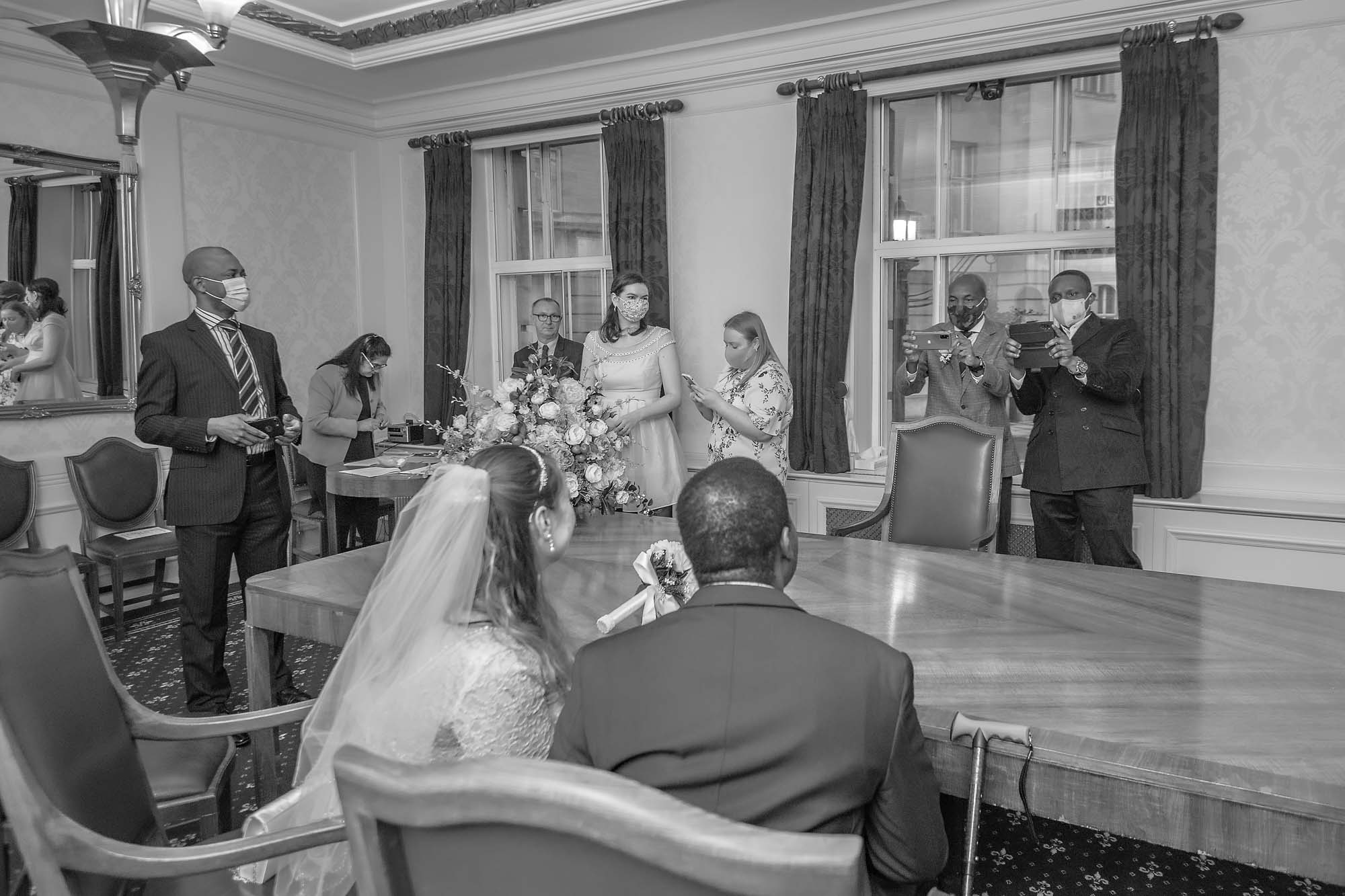 Guests take photographs of the seated couple at their register office wedding