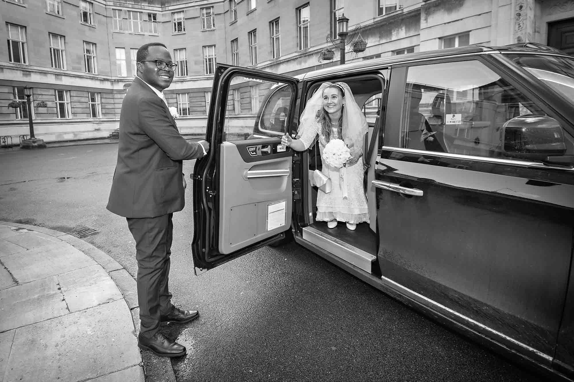 The groom holds the taxi door open for his smiling bride at Wandsworth Town Hall