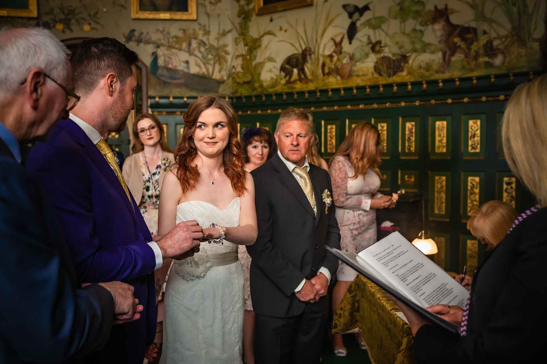 Groom places wedding ring on bride's finger at Castell Coch