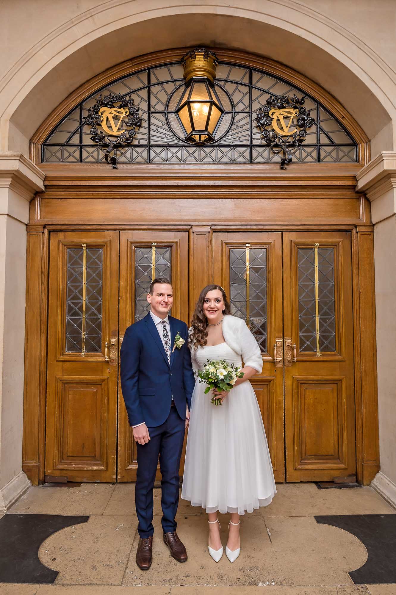 The bride and groom pose inside the front doors of Cardiff City Hall
