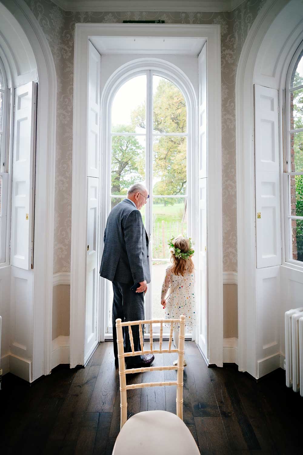 Little girl with her grandfather standing in bay windows of Morden Park house, London