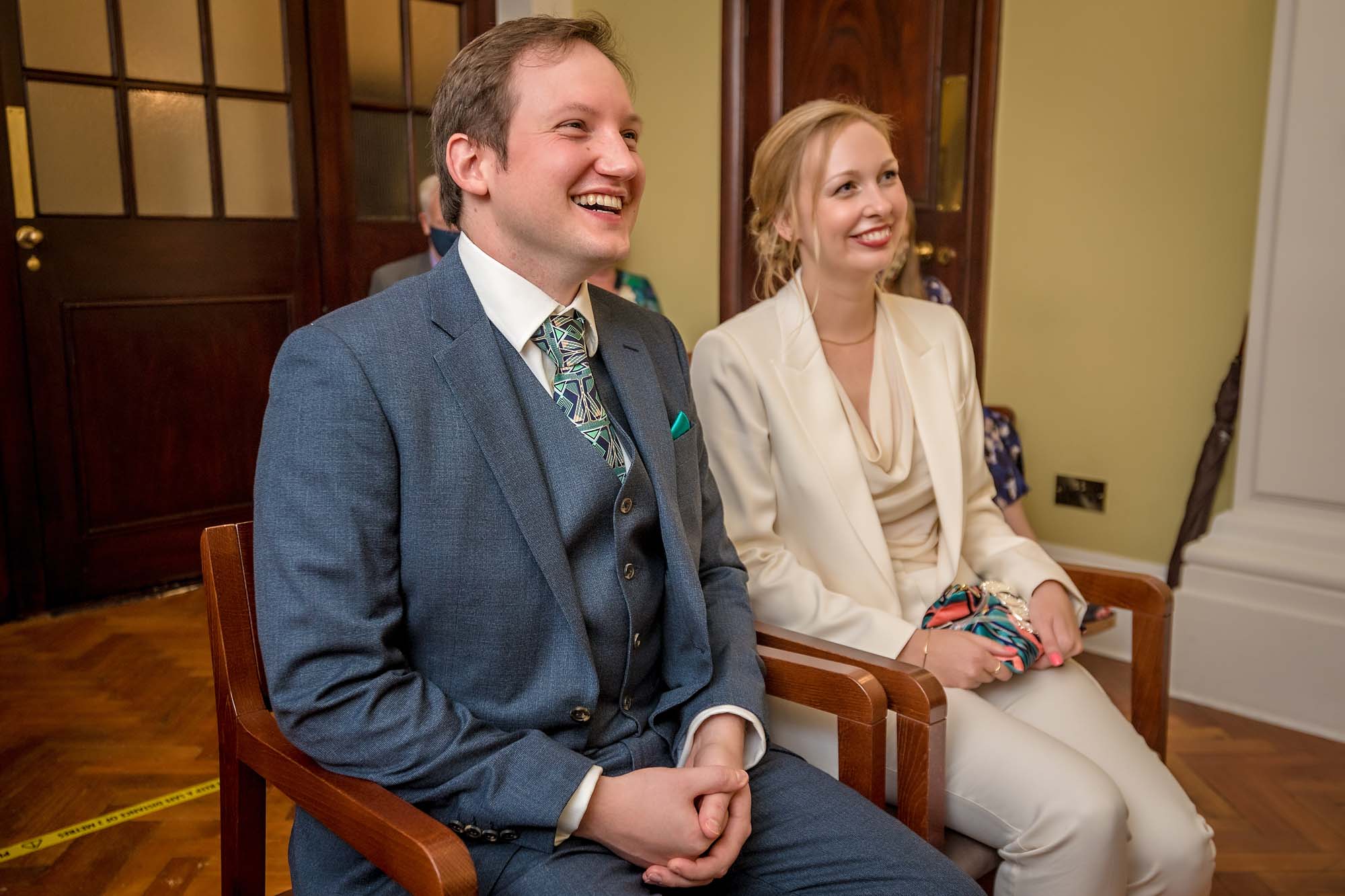 The bride and groom seated and smiling at their wedding ceremony in Chelsea Old Town Hall