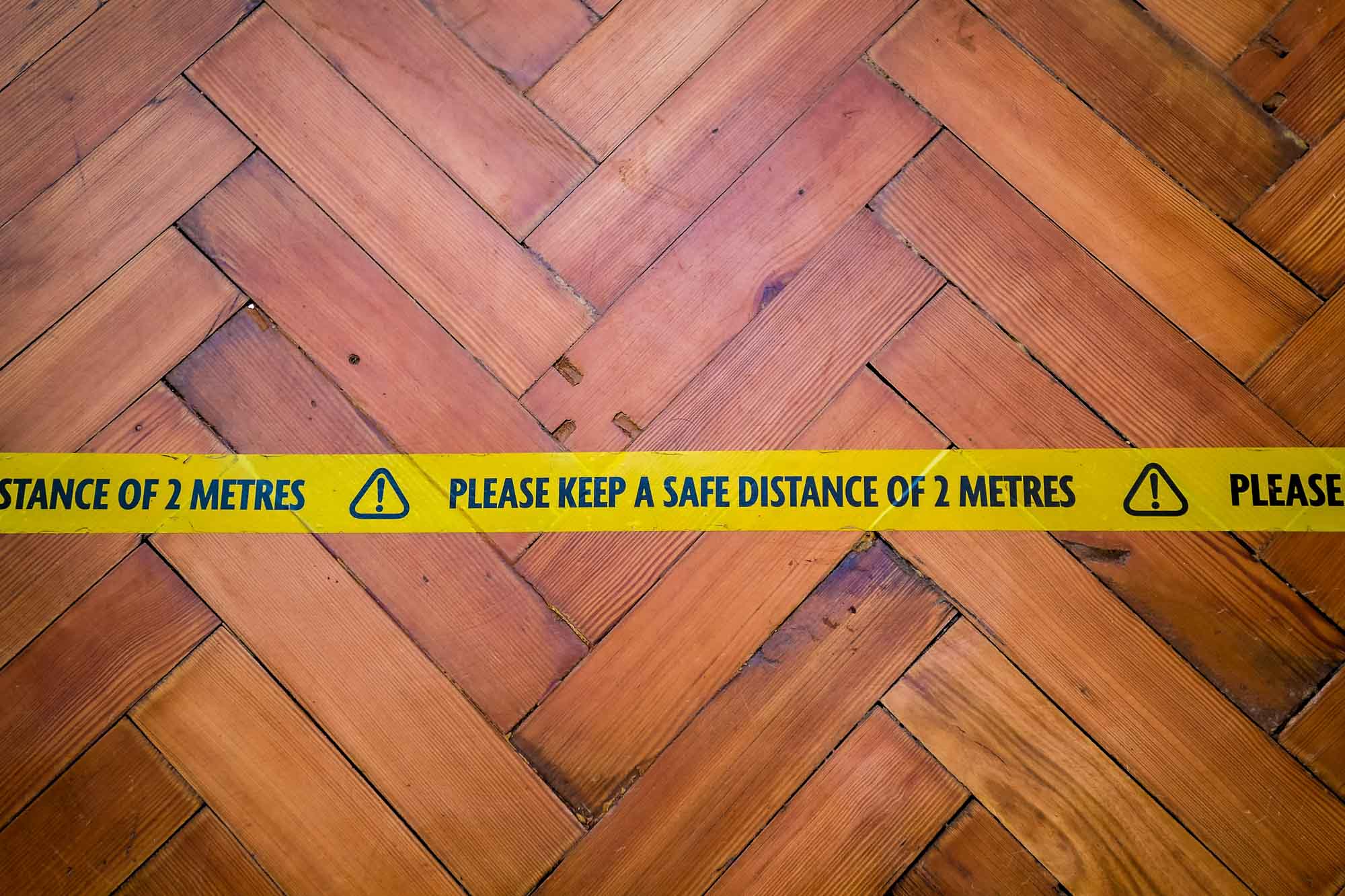 Yellow 'Please Keep a Safe Distance of 2 Metres' tape on wooden floor