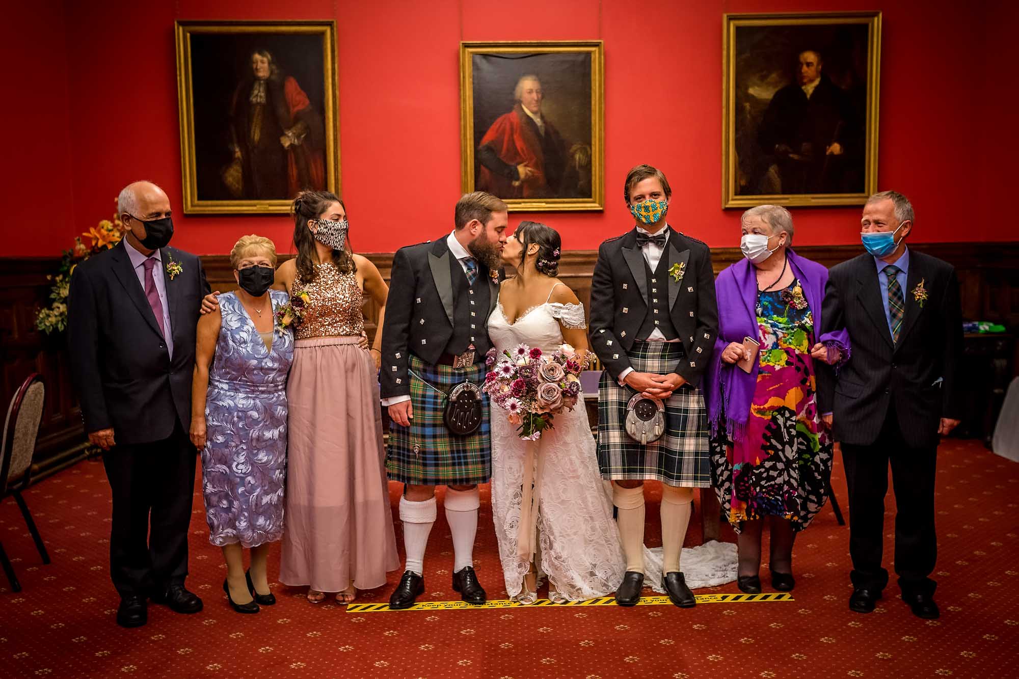 The bride and groom kiss whilst guests with face masks watch them at Coronavirus restricted wedding