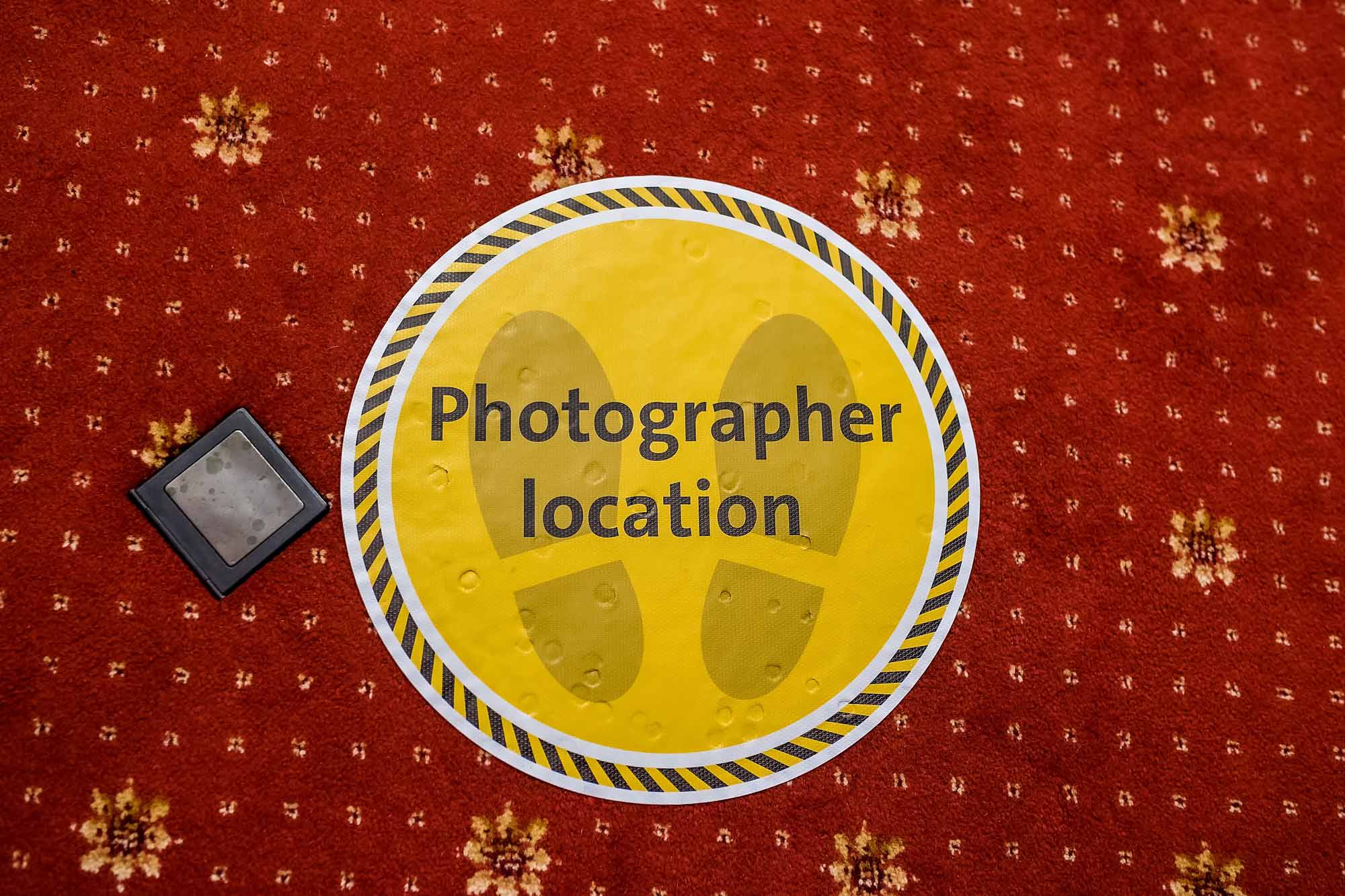 Yellow Coronavirus floor sticker at wedding venue saying 'Photographer Location'