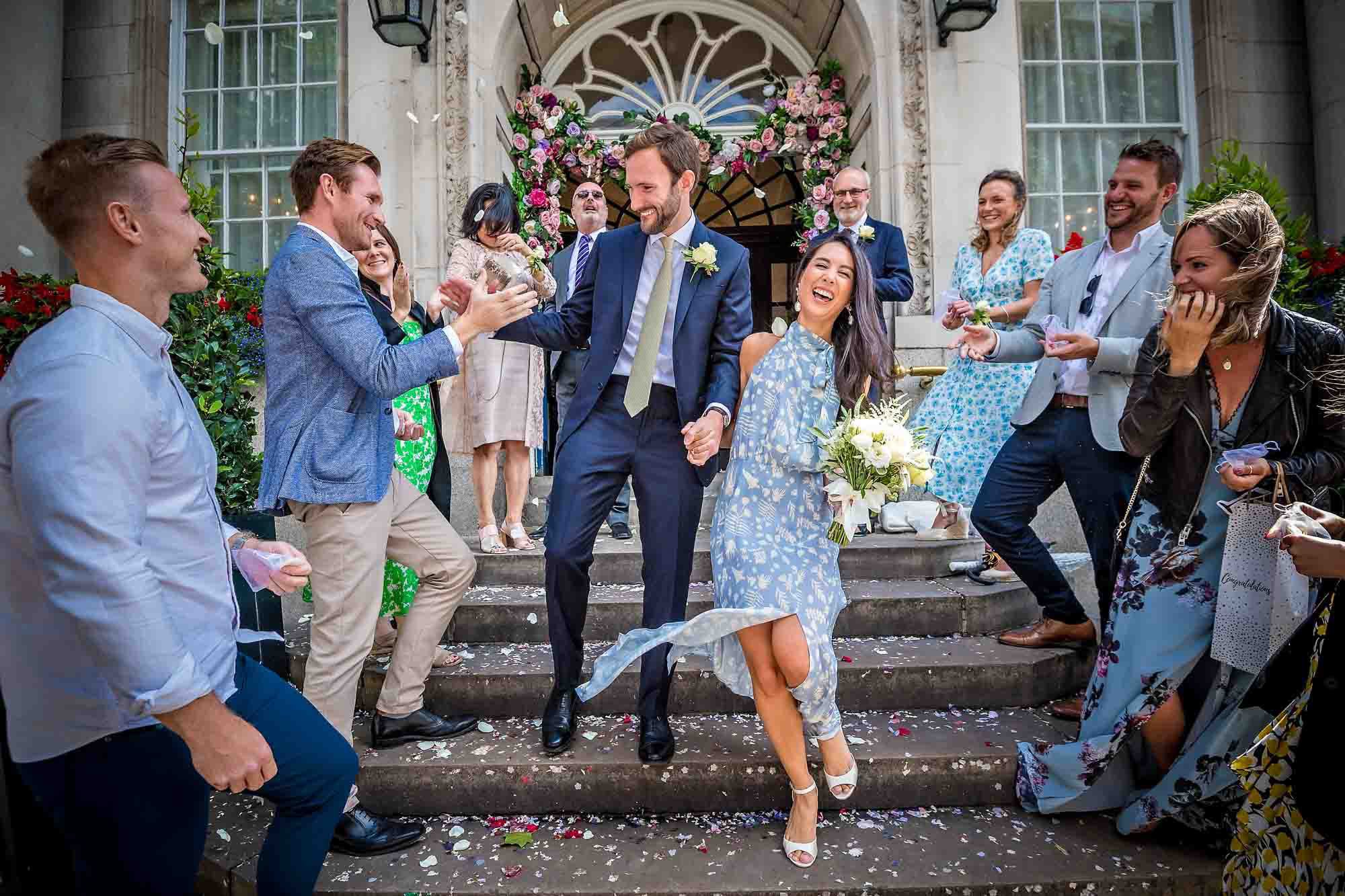 Chelsea Old Town Hall Wedding Photographer - groom greeting male guest and holding hands with bride as they leave venue